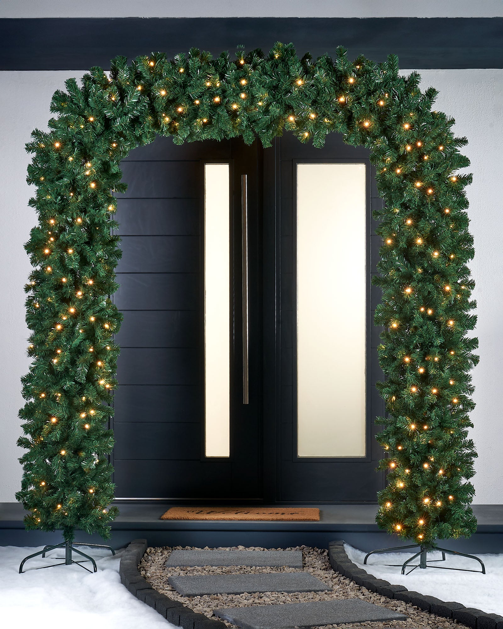 A green, pre-lit arch doorway garland with warm white LED lights displayed over a doorway, with a focus on its lifelike pine texture and the festive lighting.