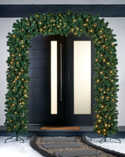 A green, pre-lit arch doorway garland with warm white LED lights displayed over a doorway, with a focus on its lifelike pine texture and the festive lighting.