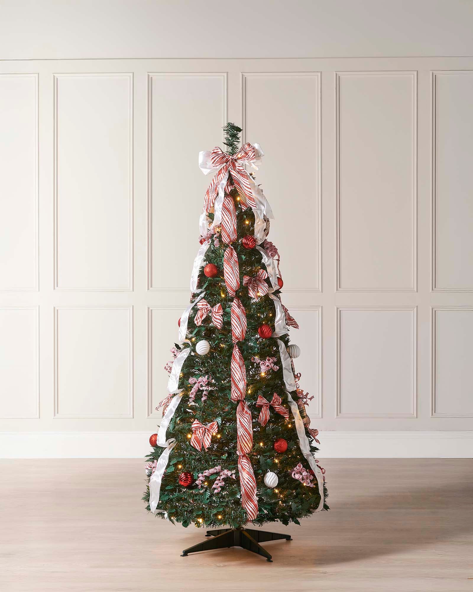 Decorated Christmas tree with ribbons and ornaments against a white paneled wall.