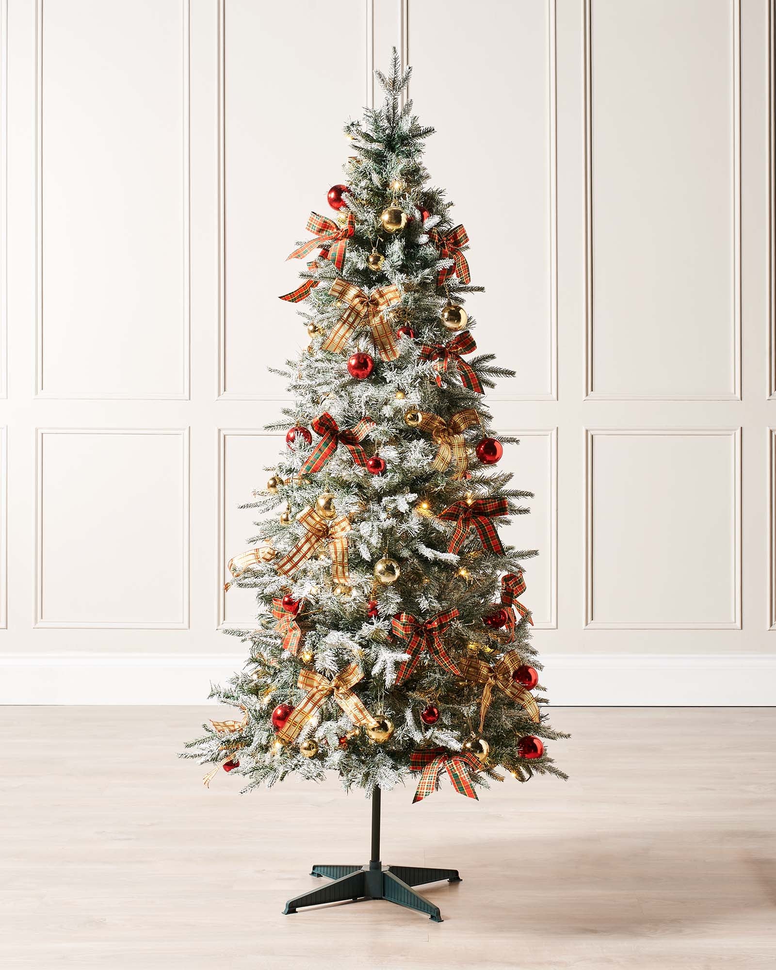 A 6-foot pre-lit pop-up artificial Christmas tree decorated with red and gold baubles and bows, featuring 100 warm white LED lights, displayed indoors with a white door in the background.