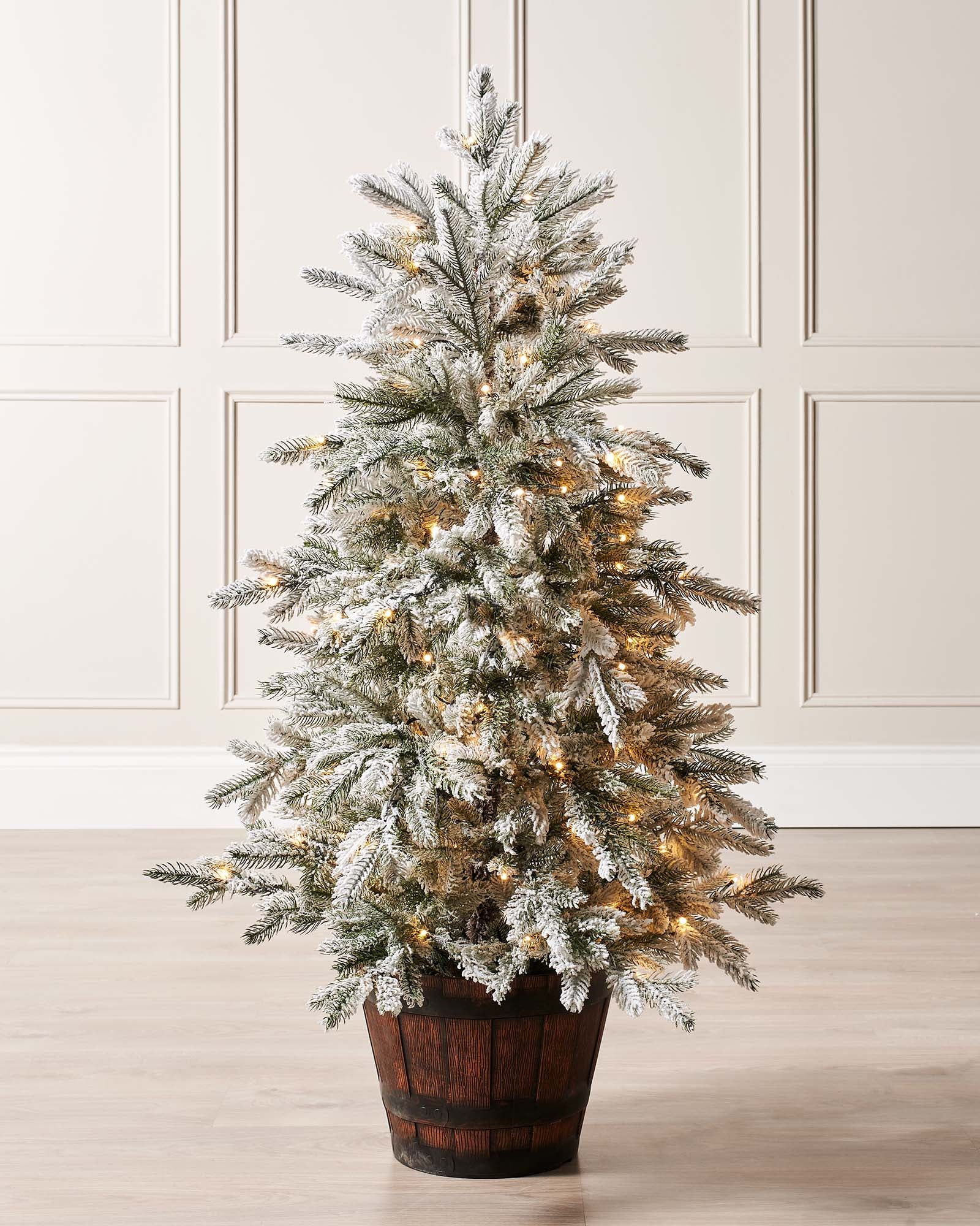 Pre-lit 4-foot snow flocked Christmas tree in a stylish pot, featuring dense mixed PE and PVC branches. Dual warm and ice white LED lights with 8 lighting modes illuminate the tree, which stands on a flexible 3-metre lead.