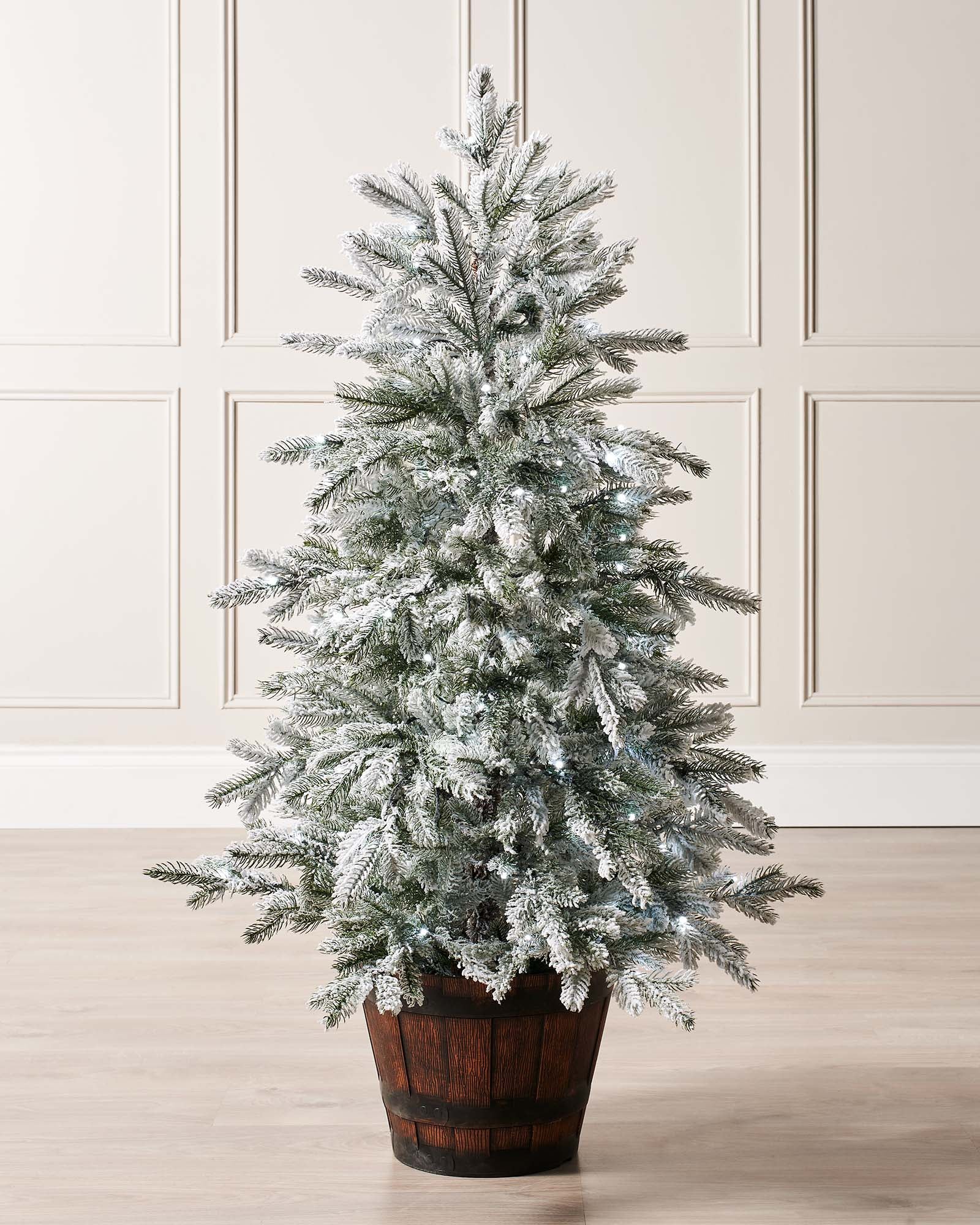 Pre-lit 4-foot snow flocked Christmas tree in a stylish pot, featuring dense mixed PE and PVC branches. Dual warm and ice white LED lights with 8 lighting modes illuminate the tree, which stands on a flexible 3-metre lead.