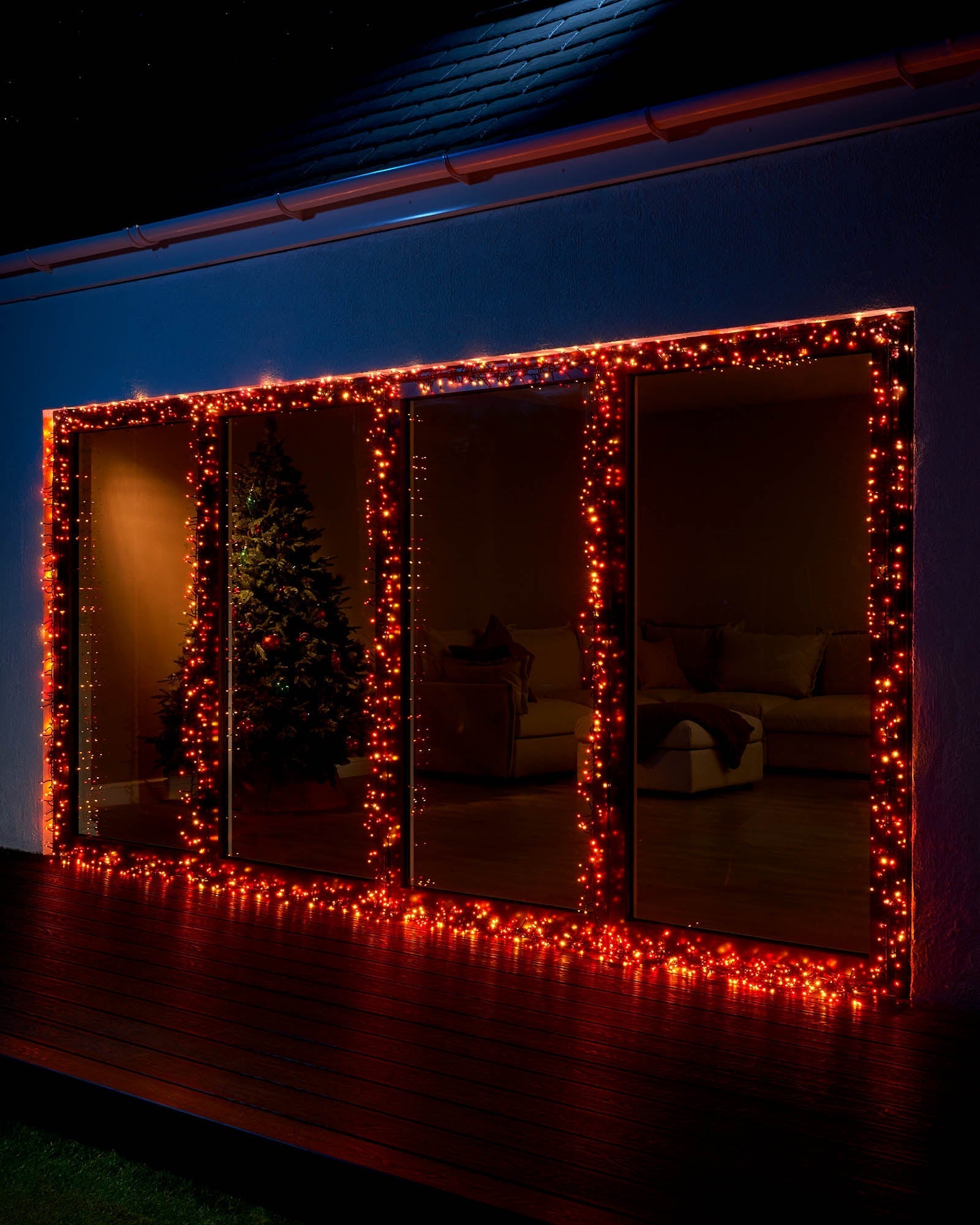 A series of connectable cluster lights glowing in orange and red hues, wrapped around a window frame, creating a warm, autumnal ambiance.