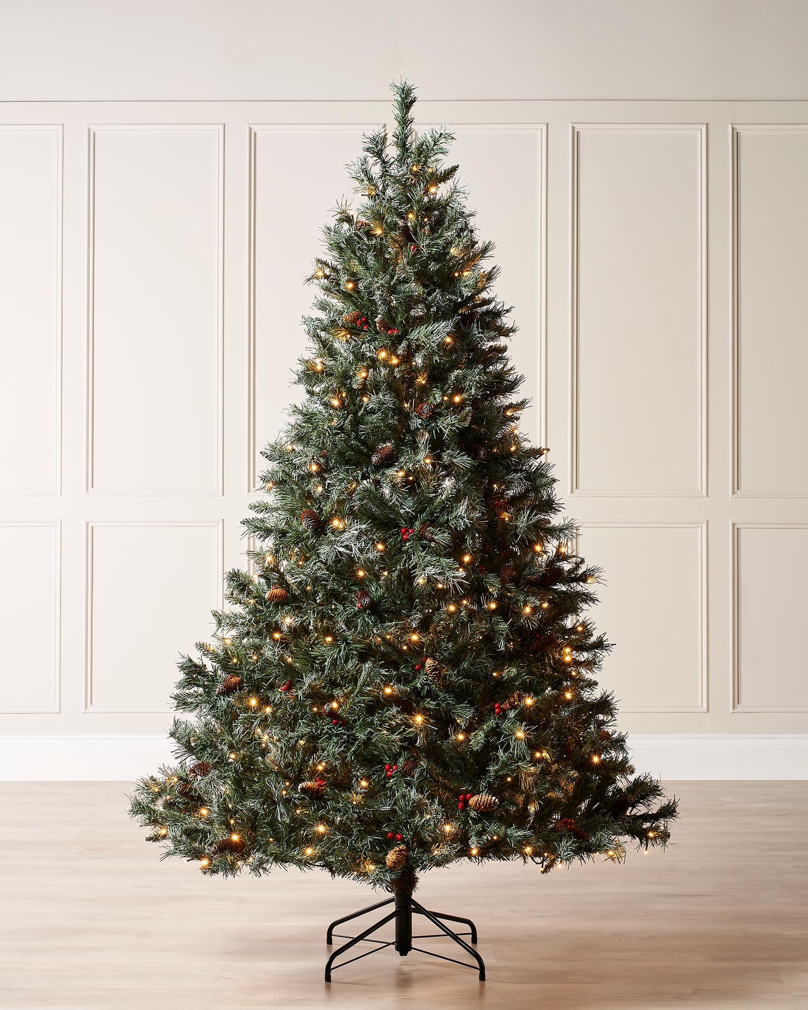A pre-lit Scandinavian spruce Christmas tree with frosted white-tipped PVC branches, warm white LED lights, natural pinecones, and red berries. Set on a sturdy metal stand, this indoor tree evokes the charm of a snowy Nordic forest.