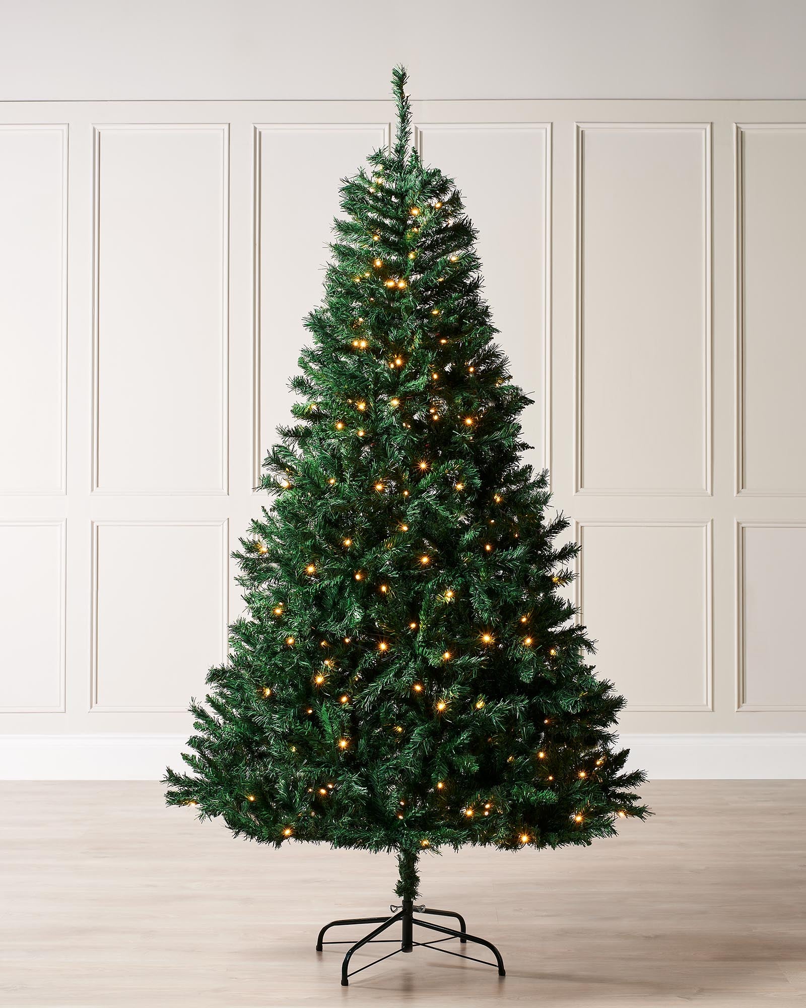 Pre-lit Mixed Pine Christmas tree with lifelike V-cut and bullet-style tips, glowing with warm white LED lights. Displayed indoors on a metal stand, featuring an 8-function memory controller and a long lead wire for flexible placement.