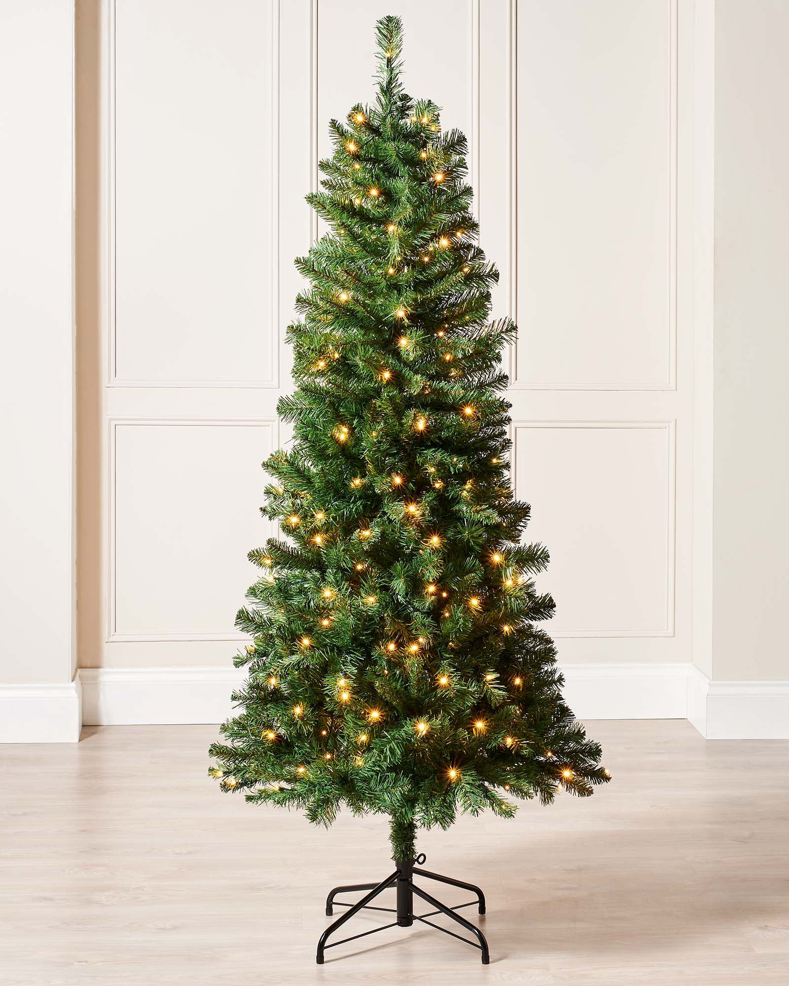 A 6 ft pre-lit slim Christmas tree featuring 508 lush PVC tips and 200 warm white LED lights, displayed indoors. The slender silhouette emits a cosy, inviting glow, ideal for adding festive charm to both compact and spacious settings.