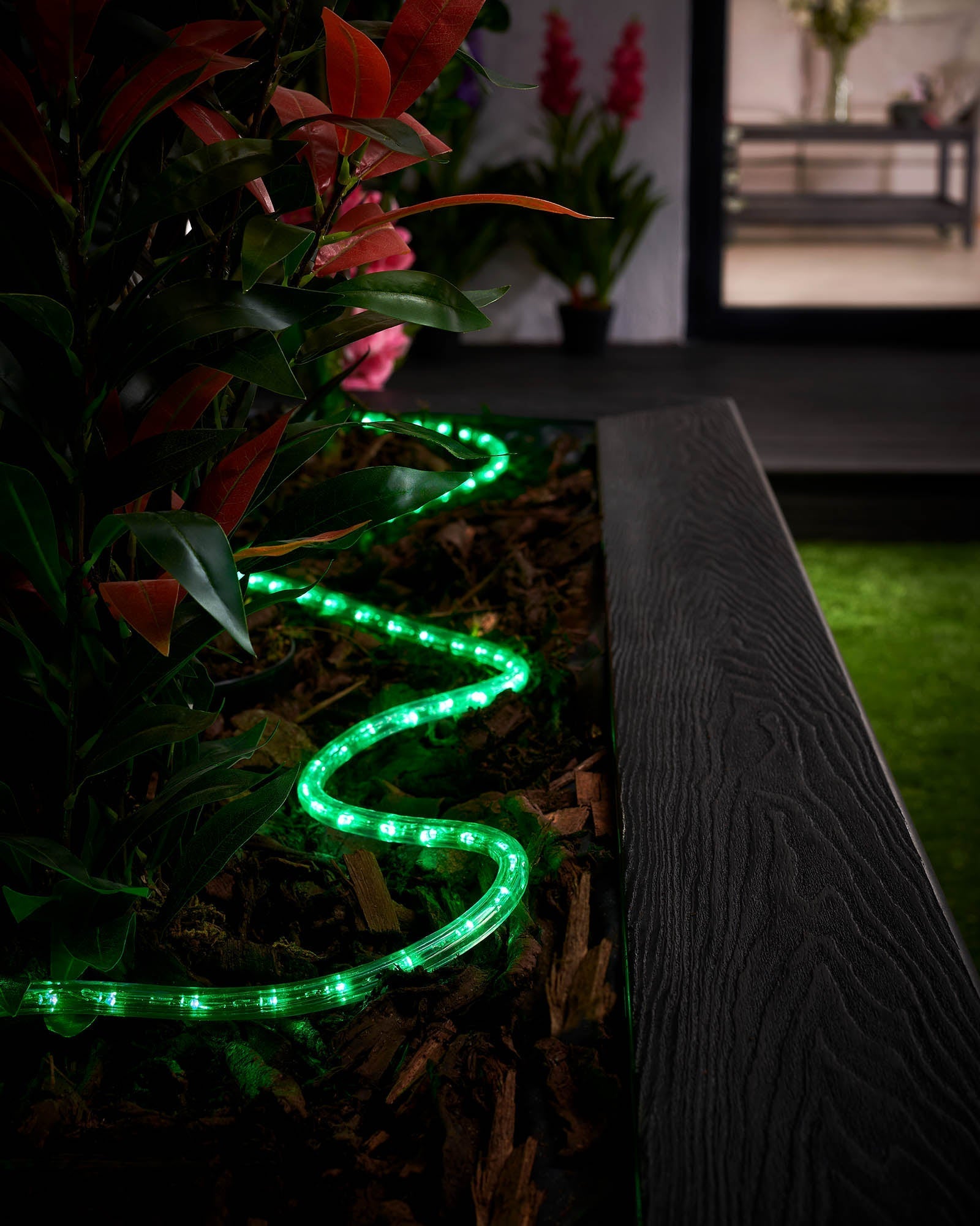 Connectable green LED rope light installed around a garden bed, displaying vibrant green lights.