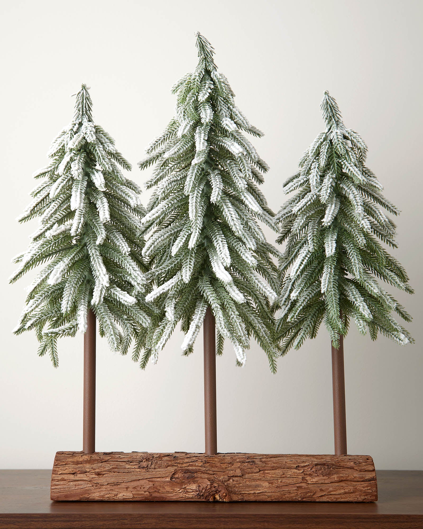 Decorative set of three artificial pine trees on a wooden base against a plain background