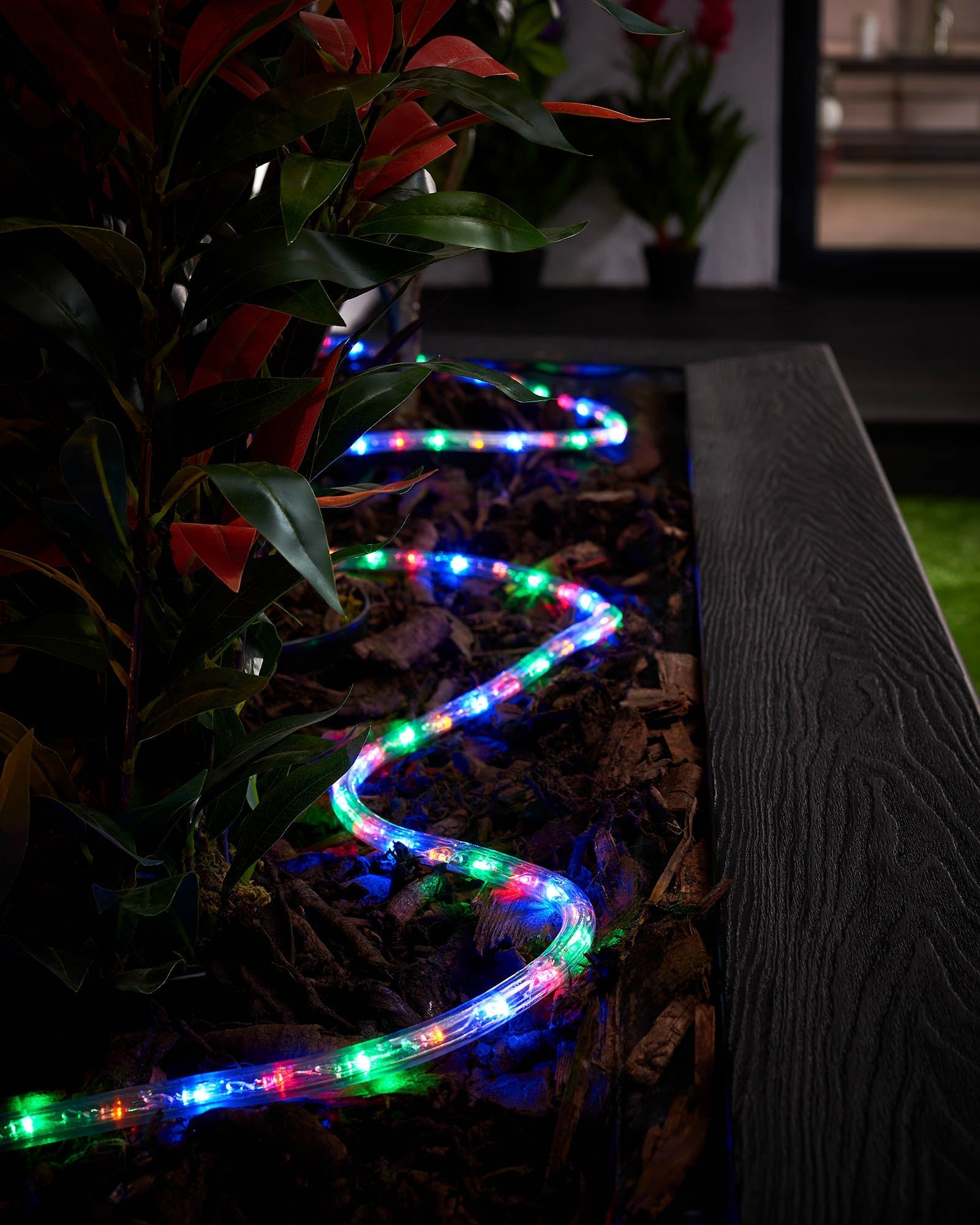 Multi-coloured LED rope lights placed along a garden bed, creating a vibrant lighting display.
