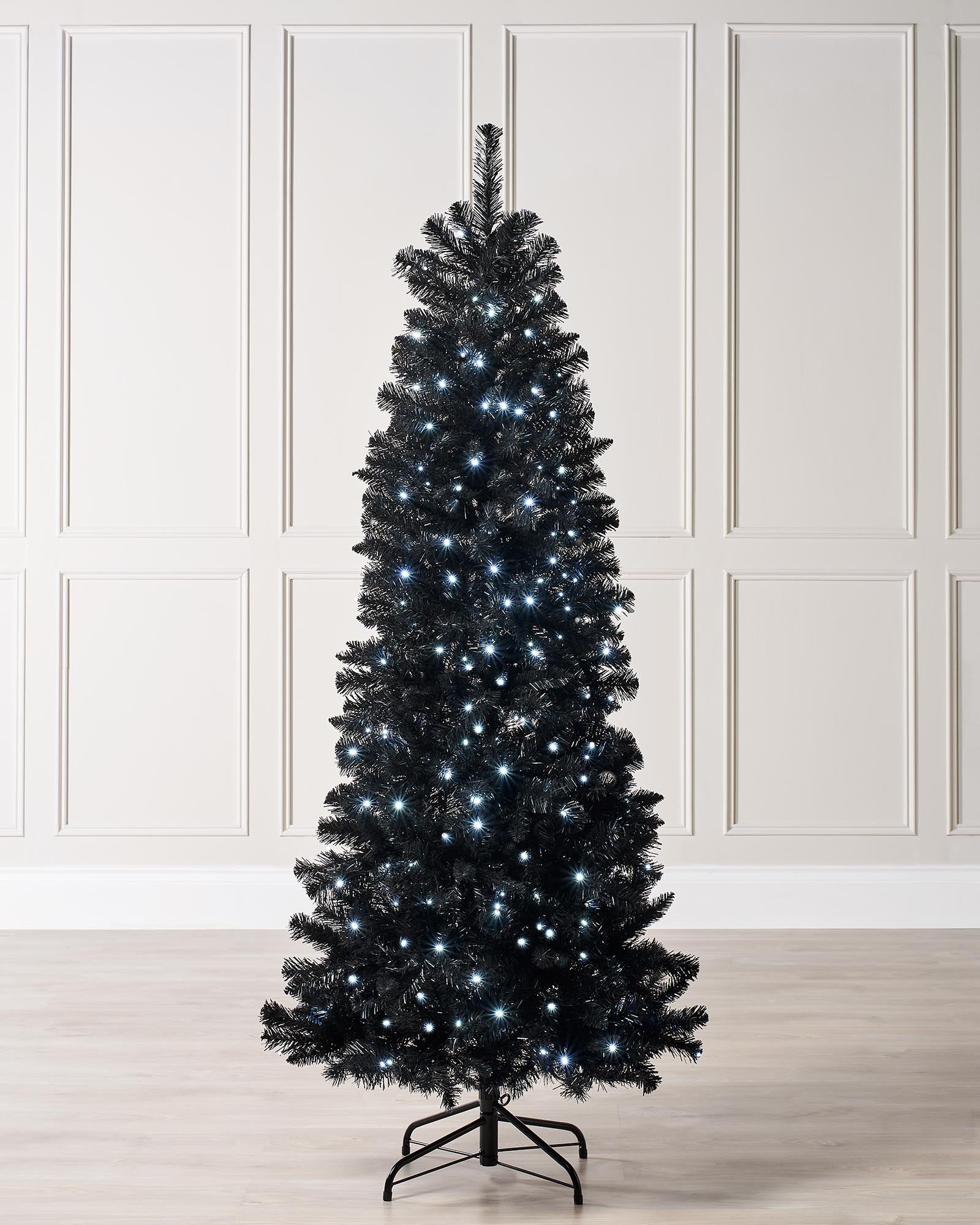 A 6 ft pre-lit slim black Christmas tree adorned with 200 cool white LED lights and 508 PVC tips, casting a frosty glow. Displayed in an indoor setting, this sleek tree brings a modern, minimalist twist to classic holiday décor.