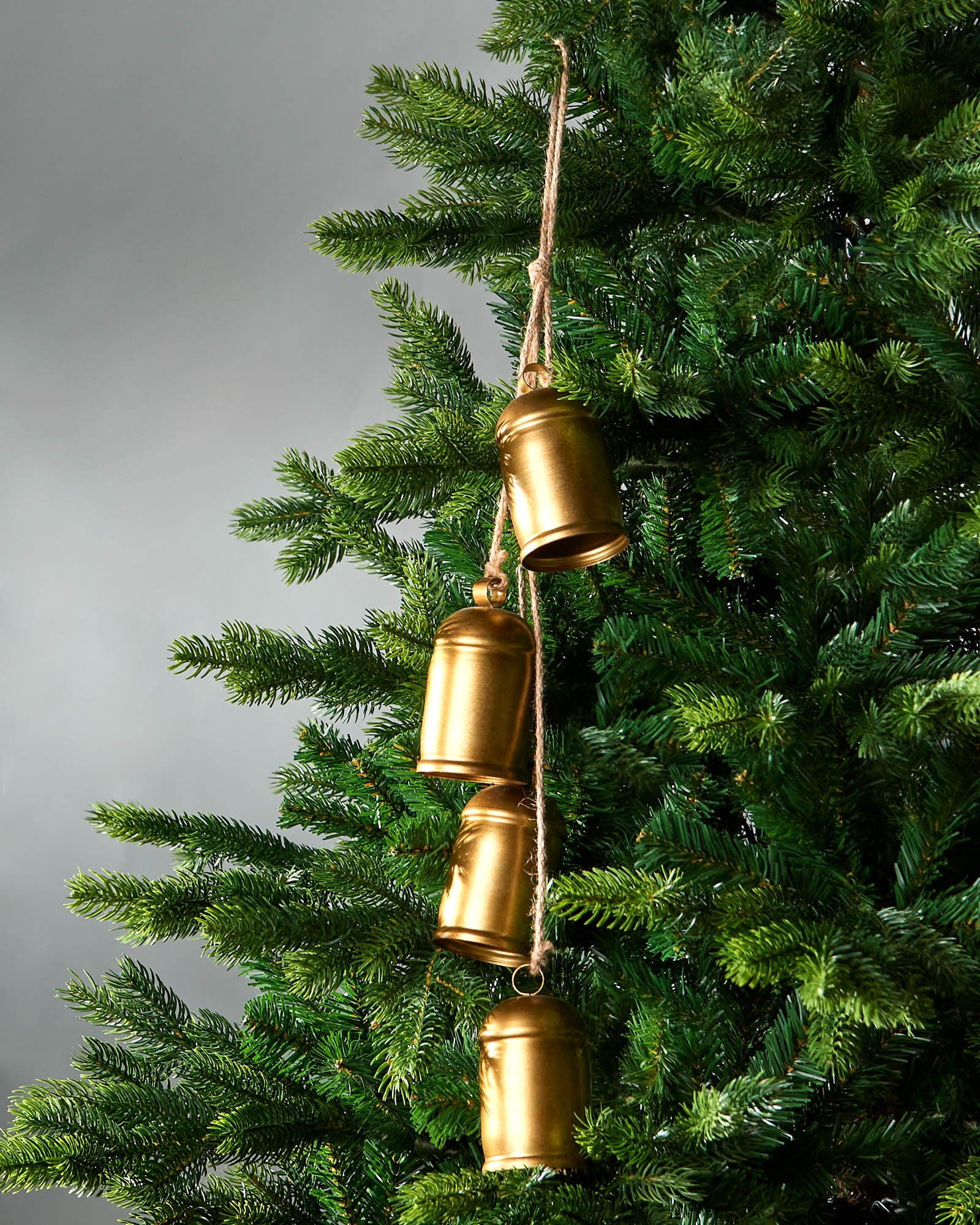 Gold bell ornament hanging on a Christmas tree against a gray background