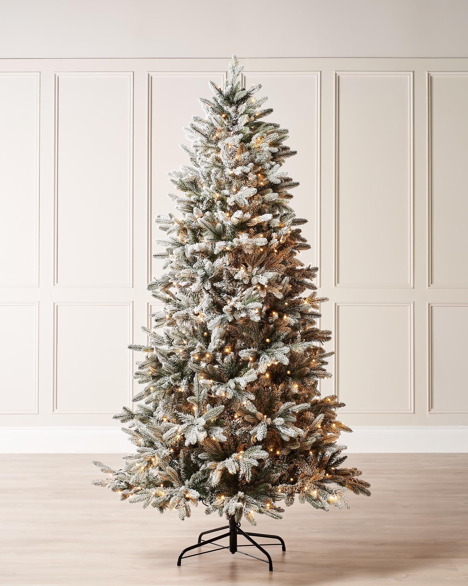 A pre-lit slim Christmas tree with snow-flocked PE and PVC branches, adorned with warm white LED lights. This elegant 6 ft tree features a slender profile and realistic snow-dusted foliage, perfect for adding a cozy winter glow to any indoor space.