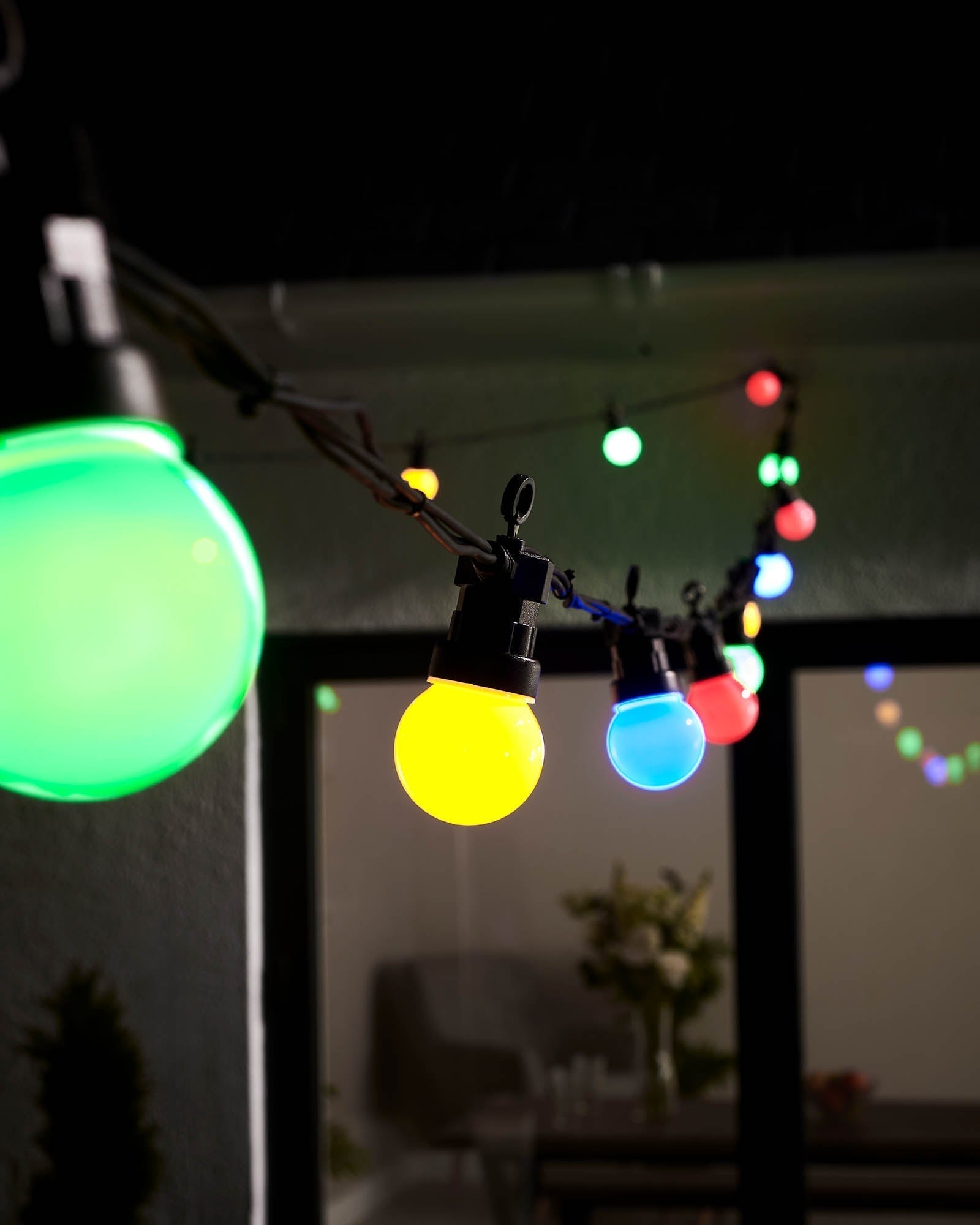 String lights with multi-colored bulbs hanging outdoors, displaying a variety of colors including green, yellow, and blue.