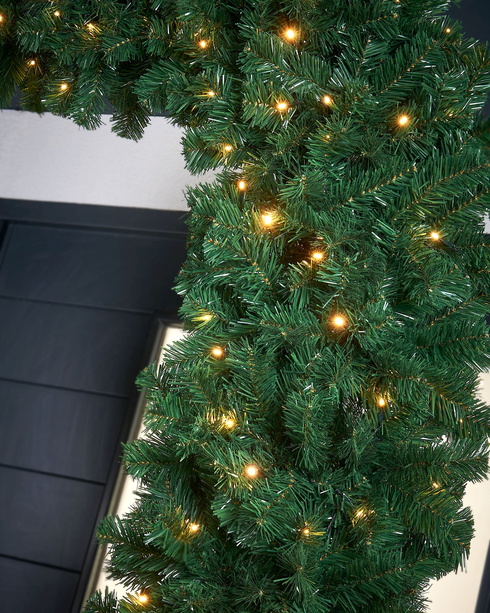 A close-up of a pre-lit, extra thick, mixed pine snow flocked garland with pinecones and berries, featuring warm white LED lights.