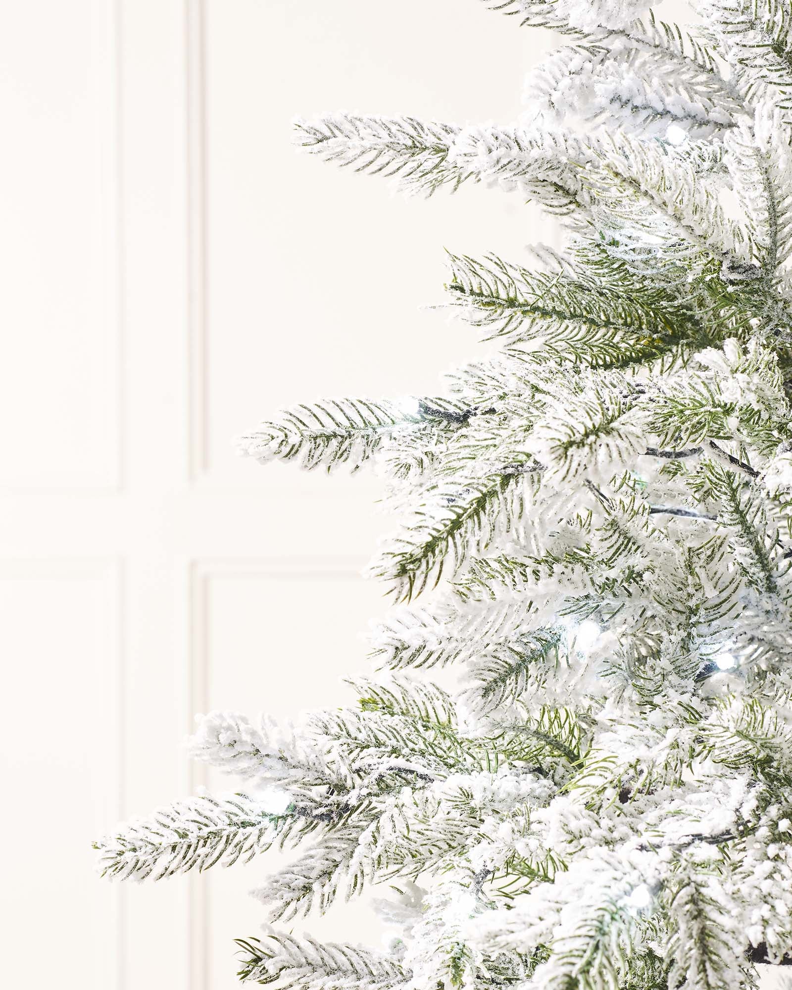 Pre-lit 4-foot snow flocked Christmas tree in a stylish pot, featuring dense mixed PE and PVC branches. Dual warm and ice white LED lights with 8 lighting modes illuminate the tree, which stands on a flexible 3-metre lead.