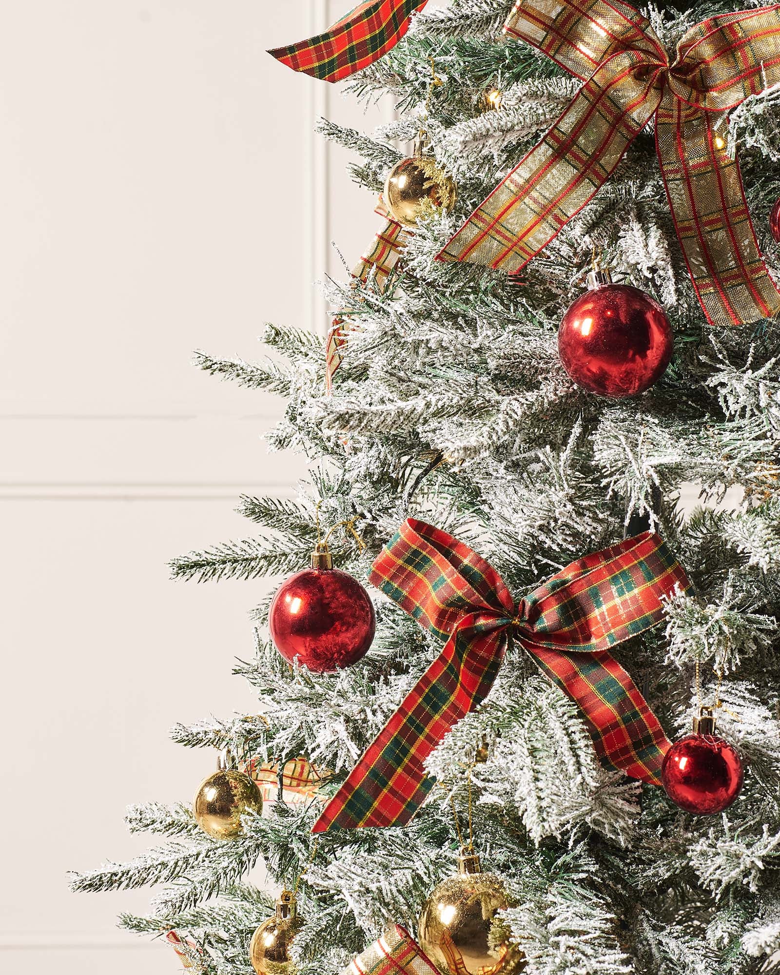 A 6-foot pre-lit pop-up artificial Christmas tree decorated with red and gold baubles and bows, featuring 100 warm white LED lights, displayed indoors with a white door in the background.