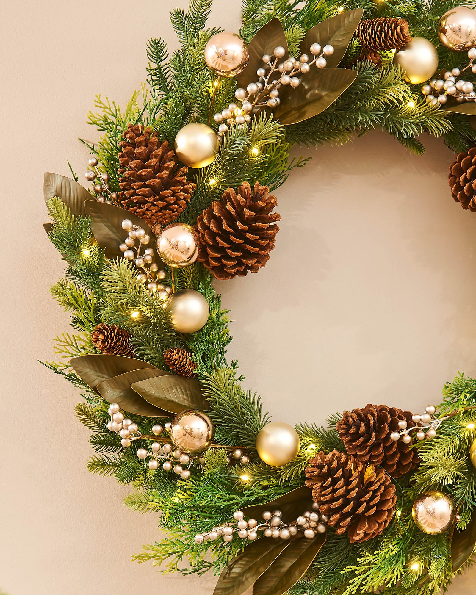 A festive Christmas wreath adorned with pinecones, gold berries, and LED lights, set against a white background.