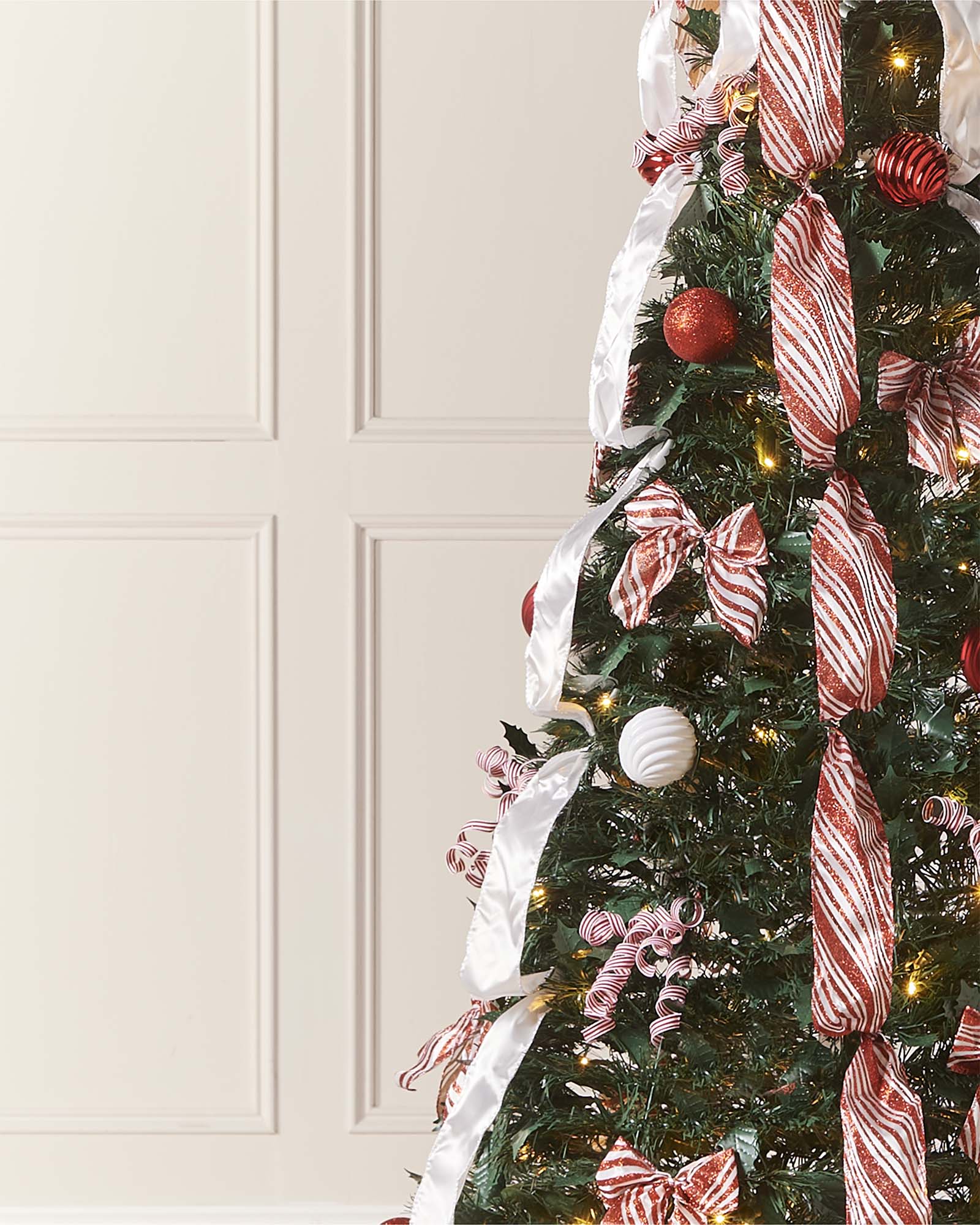 Decorated Christmas tree with ribbons and ornaments against a white paneled wall.