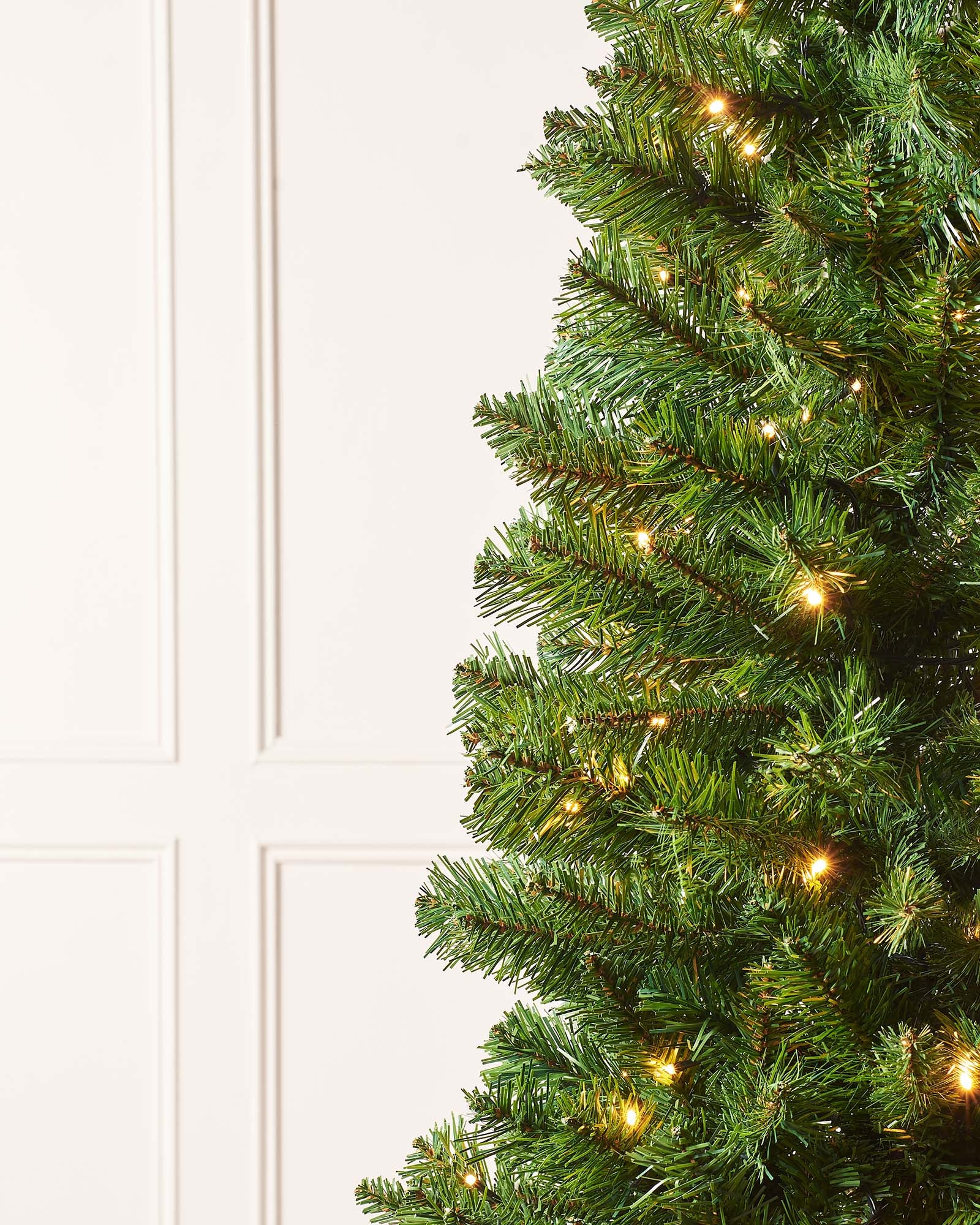 A 6 ft pre-lit slim Christmas tree featuring 508 lush PVC tips and 200 warm white LED lights, displayed indoors. The slender silhouette emits a cosy, inviting glow, ideal for adding festive charm to both compact and spacious settings.