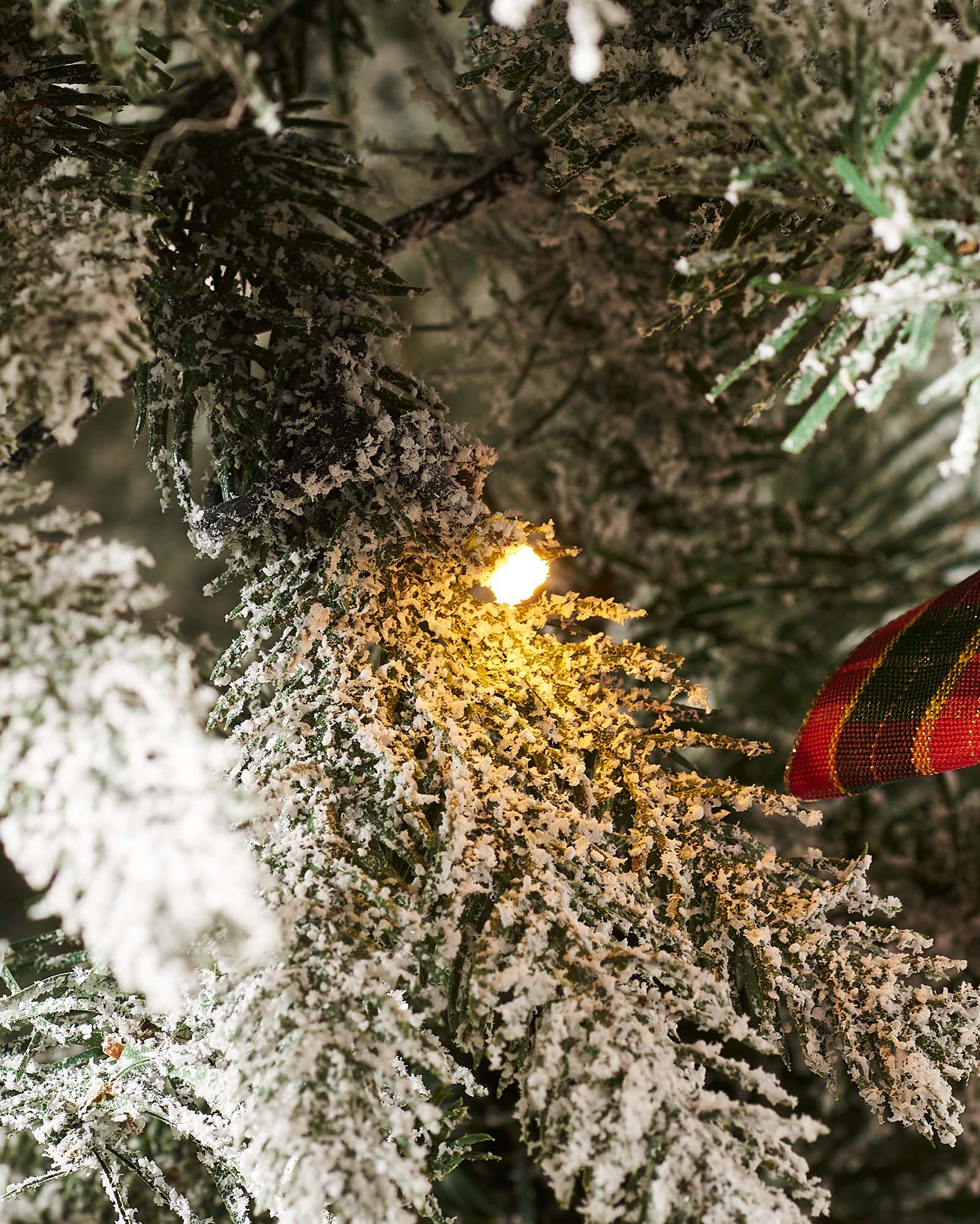 A 6-foot pre-lit pop-up artificial Christmas tree decorated with red and gold baubles and bows, featuring 100 warm white LED lights, displayed indoors with a white door in the background.