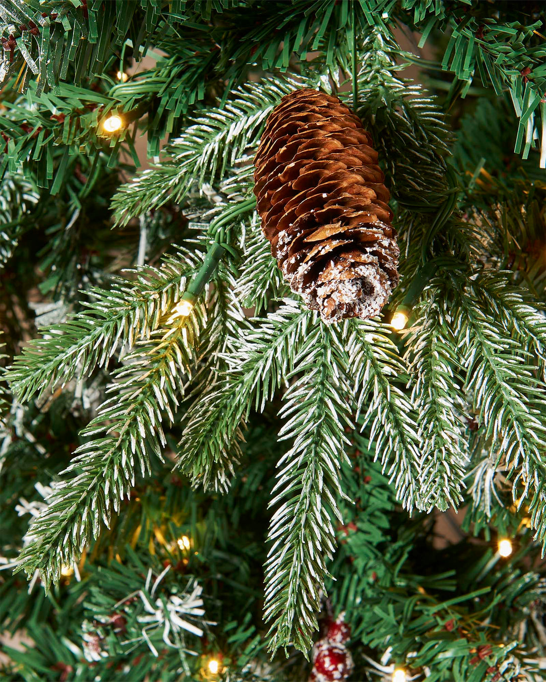 Pre-lit frosted Norwegian Spruce Christmas tree with snow-dusted branches, natural pinecones, and red berries. Features warm white multi-function LED lights and a lifelike PE and PVC tip construction.