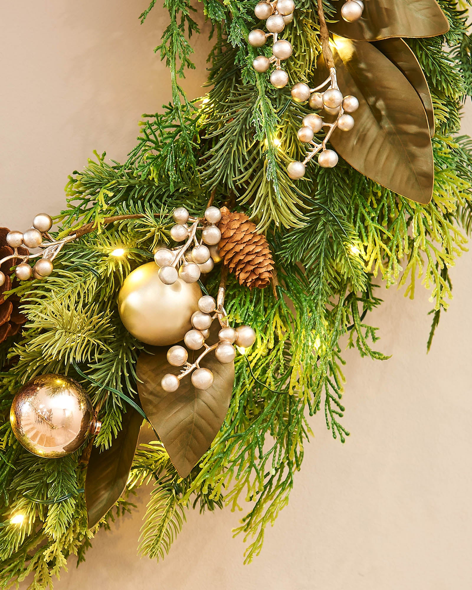 A festive Christmas wreath adorned with pinecones, gold berries, and LED lights, set against a white background.