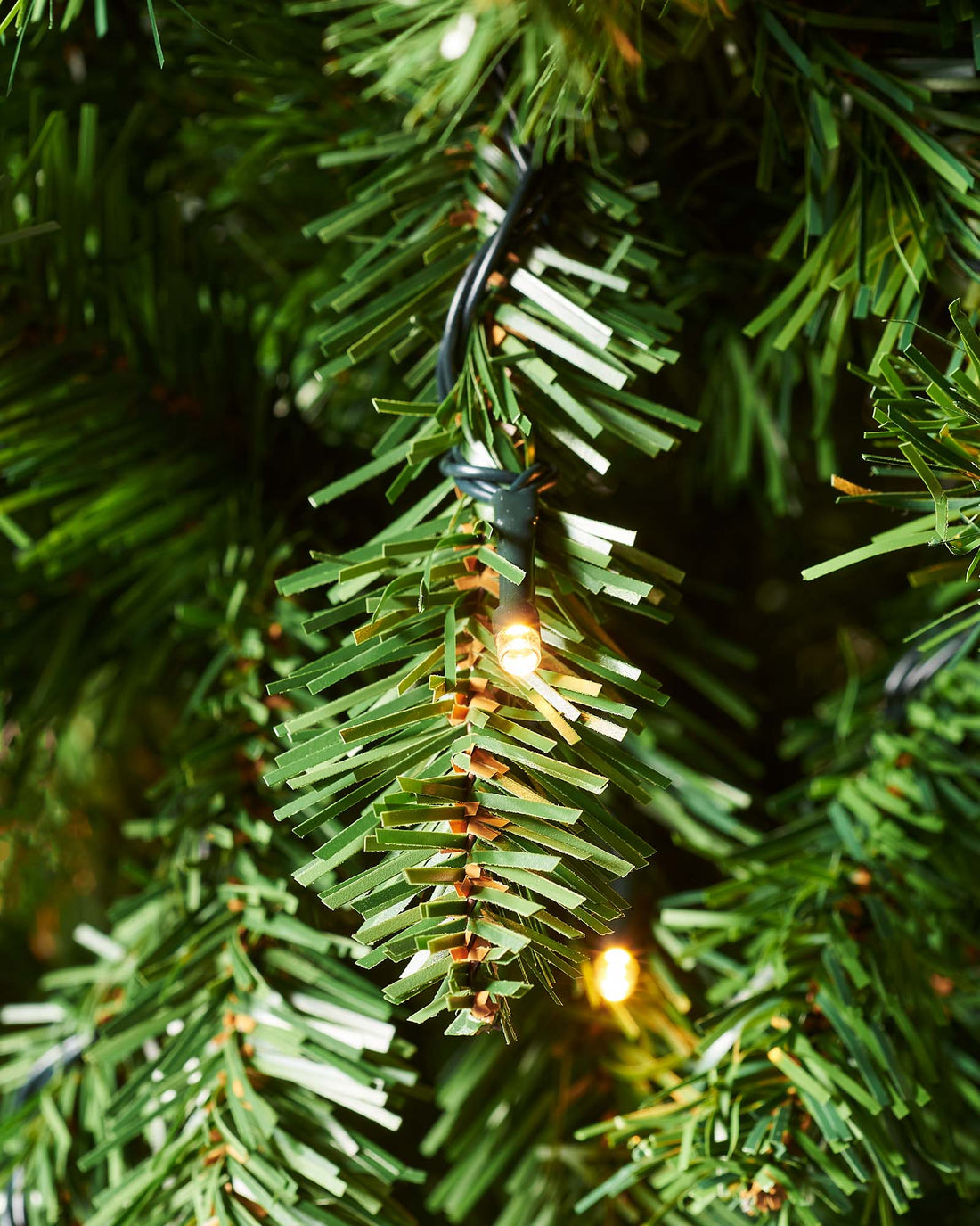 A 6 ft pre-lit slim Christmas tree featuring 508 lush PVC tips and 200 warm white LED lights, displayed indoors. The slender silhouette emits a cosy, inviting glow, ideal for adding festive charm to both compact and spacious settings.