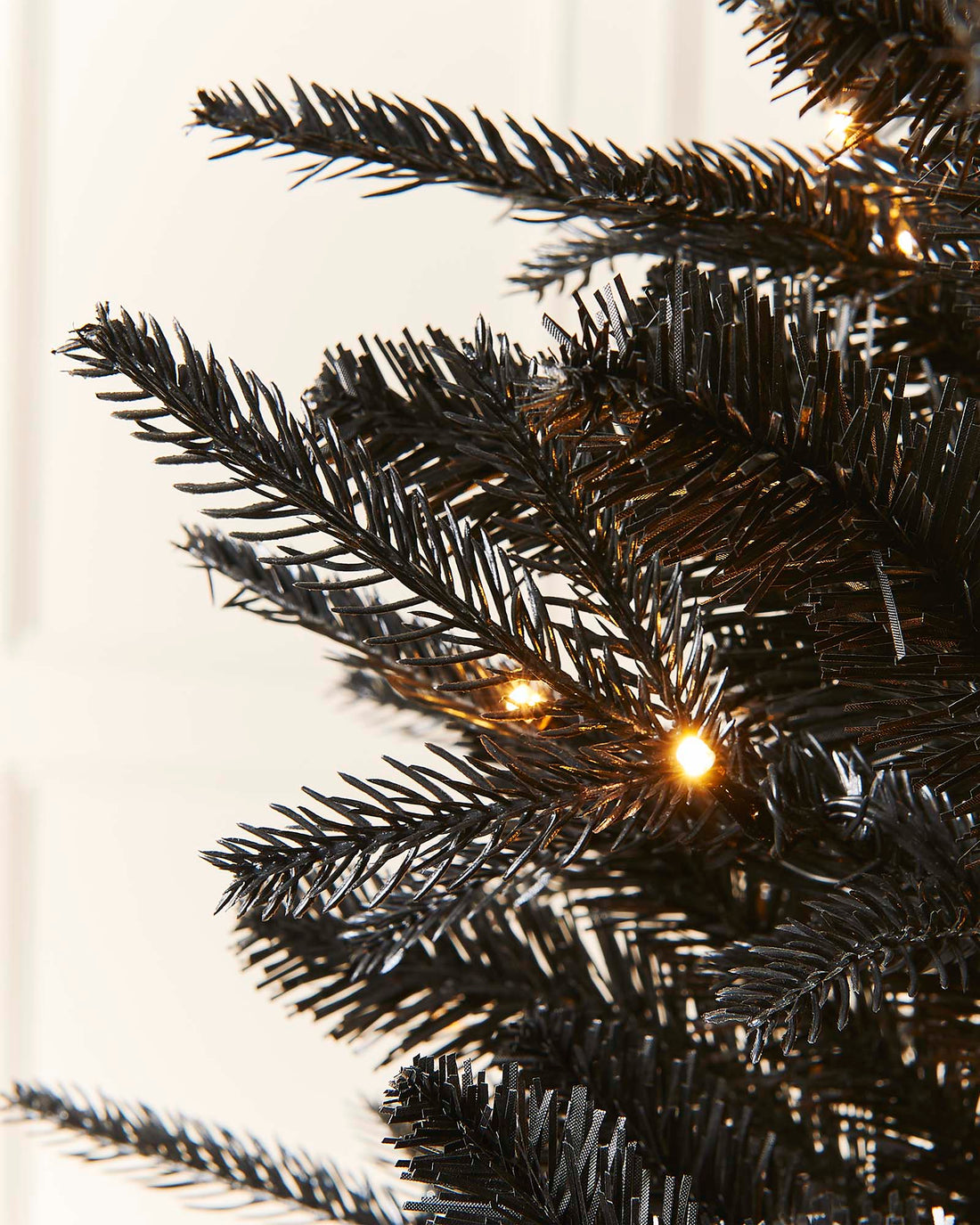 Close-up of a black Christmas tree with silver stars on a neutral background.