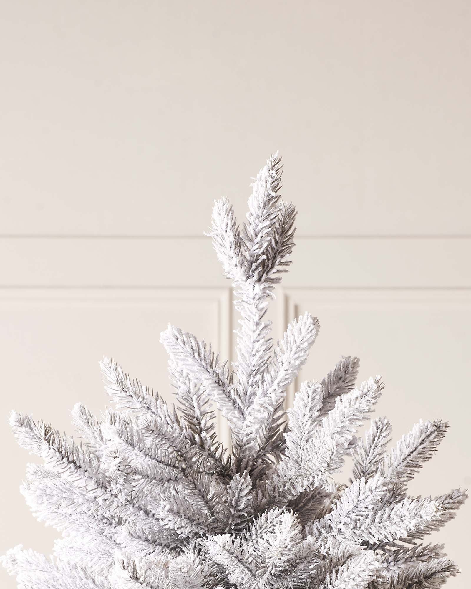 Snow-flocked grey fir artificial Christmas tree with soft grey tones, mixed tips, and a foldable metal stand—featuring a frosted, wintry look that blends traditional charm with modern elegance, perfect for stylish indoor holiday displays.