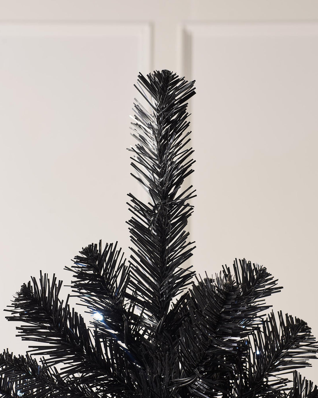 A 6 ft pre-lit slim black Christmas tree adorned with 200 cool white LED lights and 508 PVC tips, casting a frosty glow. Displayed in an indoor setting, this sleek tree brings a modern, minimalist twist to classic holiday décor.