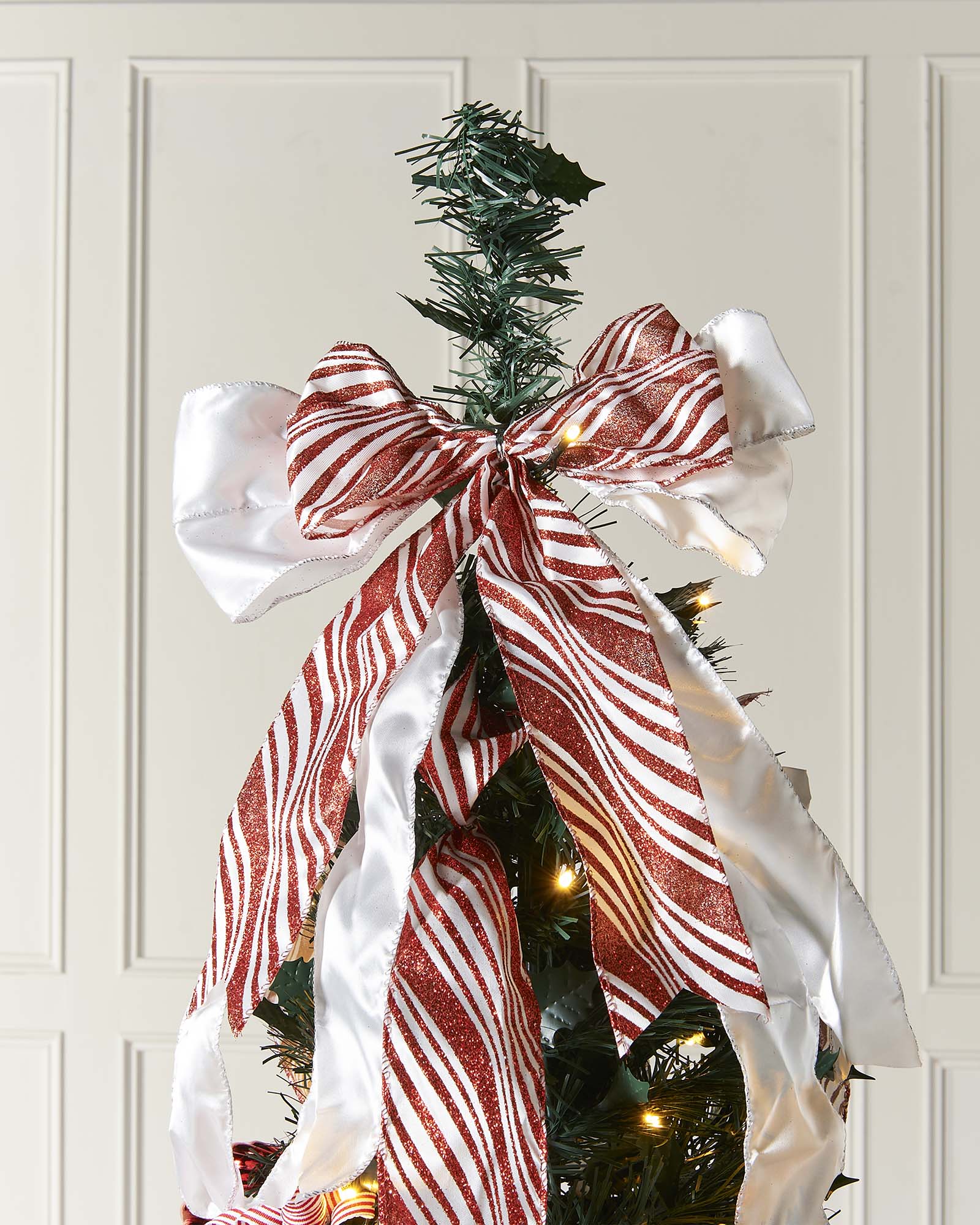 Decorated Christmas tree with ribbons and ornaments against a white paneled wall.