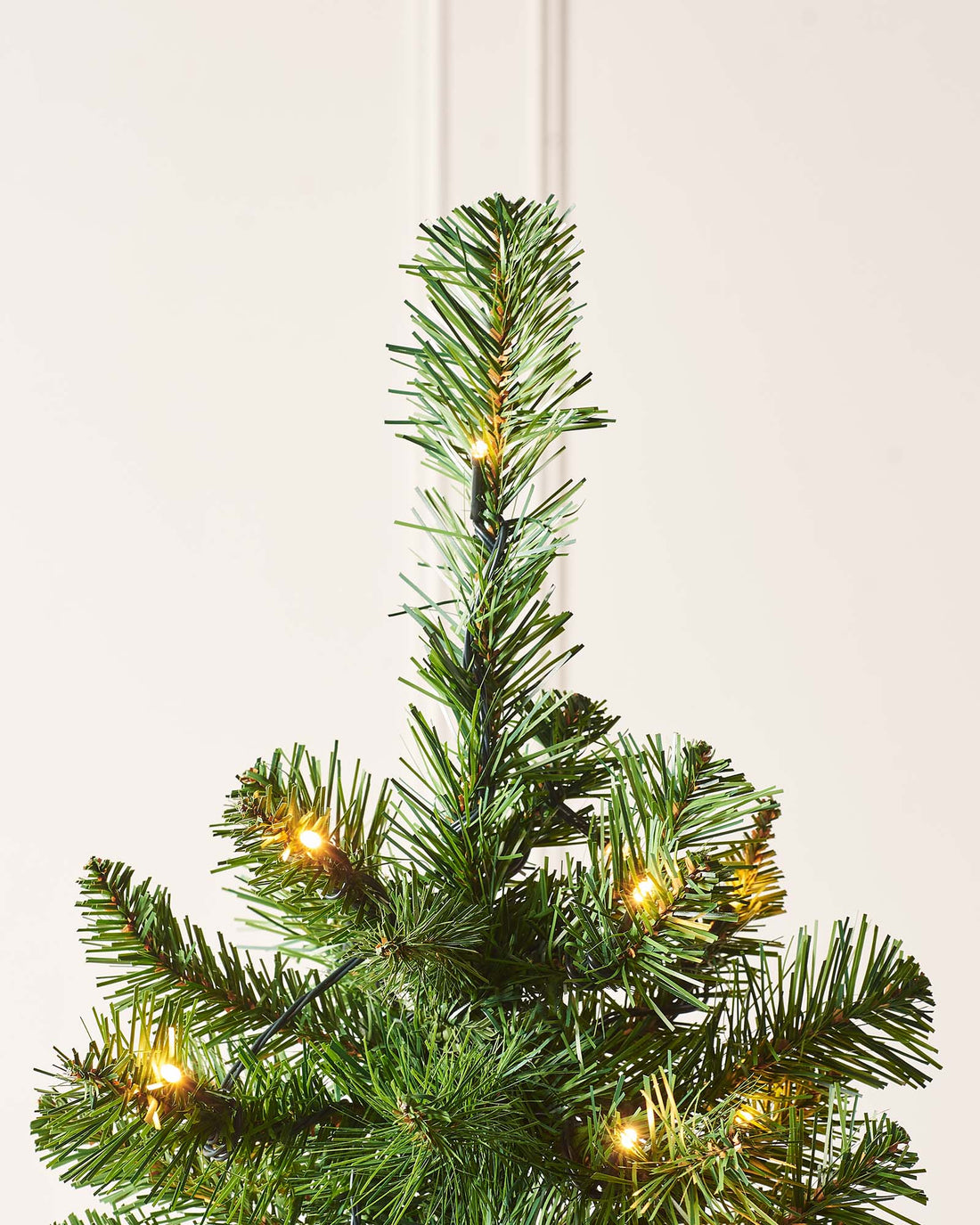 A 6 ft pre-lit slim Christmas tree featuring 508 lush PVC tips and 200 warm white LED lights, displayed indoors. The slender silhouette emits a cosy, inviting glow, ideal for adding festive charm to both compact and spacious settings.