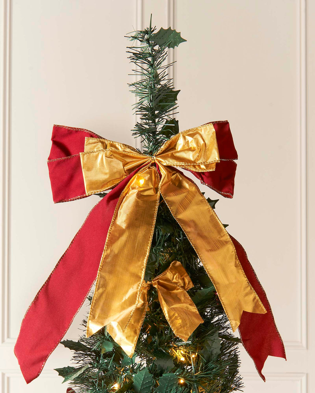 A 6-foot pre-lit pop-up Christmas tree decorated with red and gold baubles, ribbons, and flowers, featuring 150 warm white LED lights, displayed indoors against a white wall.
