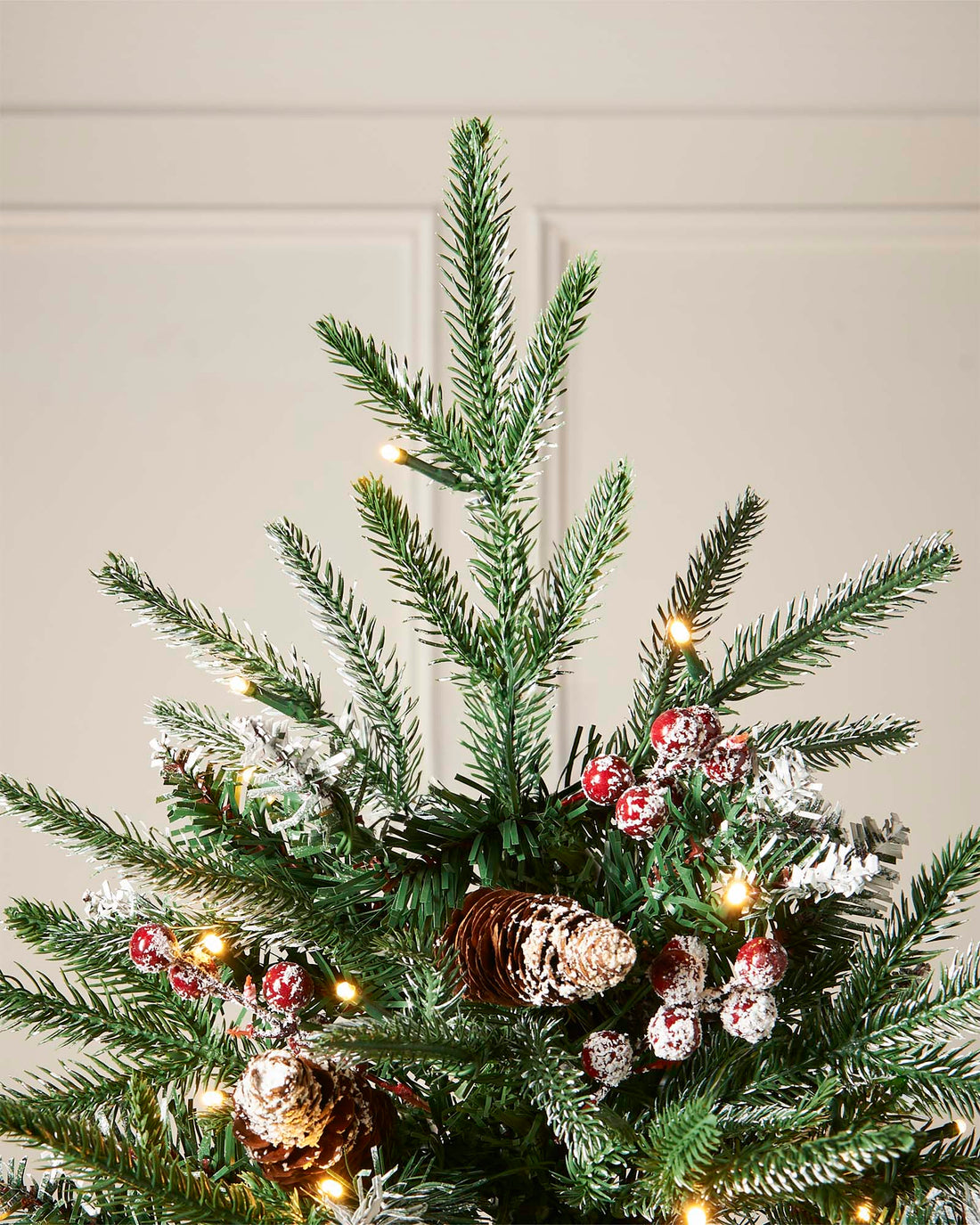 Pre-lit frosted Norwegian Spruce Christmas tree with snow-dusted branches, natural pinecones, and red berries. Features warm white multi-function LED lights and a lifelike PE and PVC tip construction.