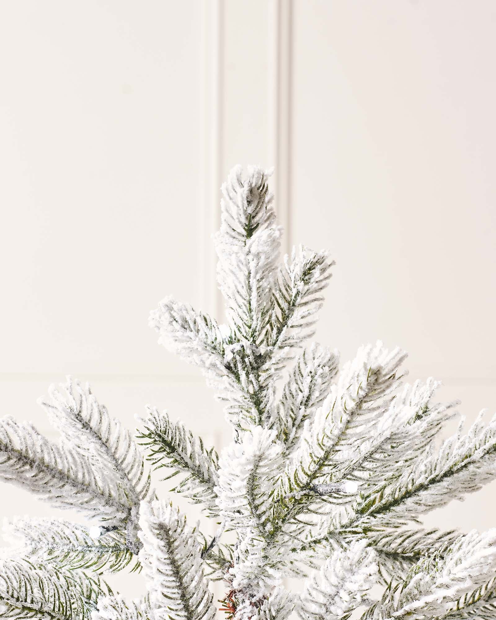 Pre-lit 4-foot snow flocked Christmas tree in a stylish pot, featuring dense mixed PE and PVC branches. Dual warm and ice white LED lights with 8 lighting modes illuminate the tree, which stands on a flexible 3-metre lead.
