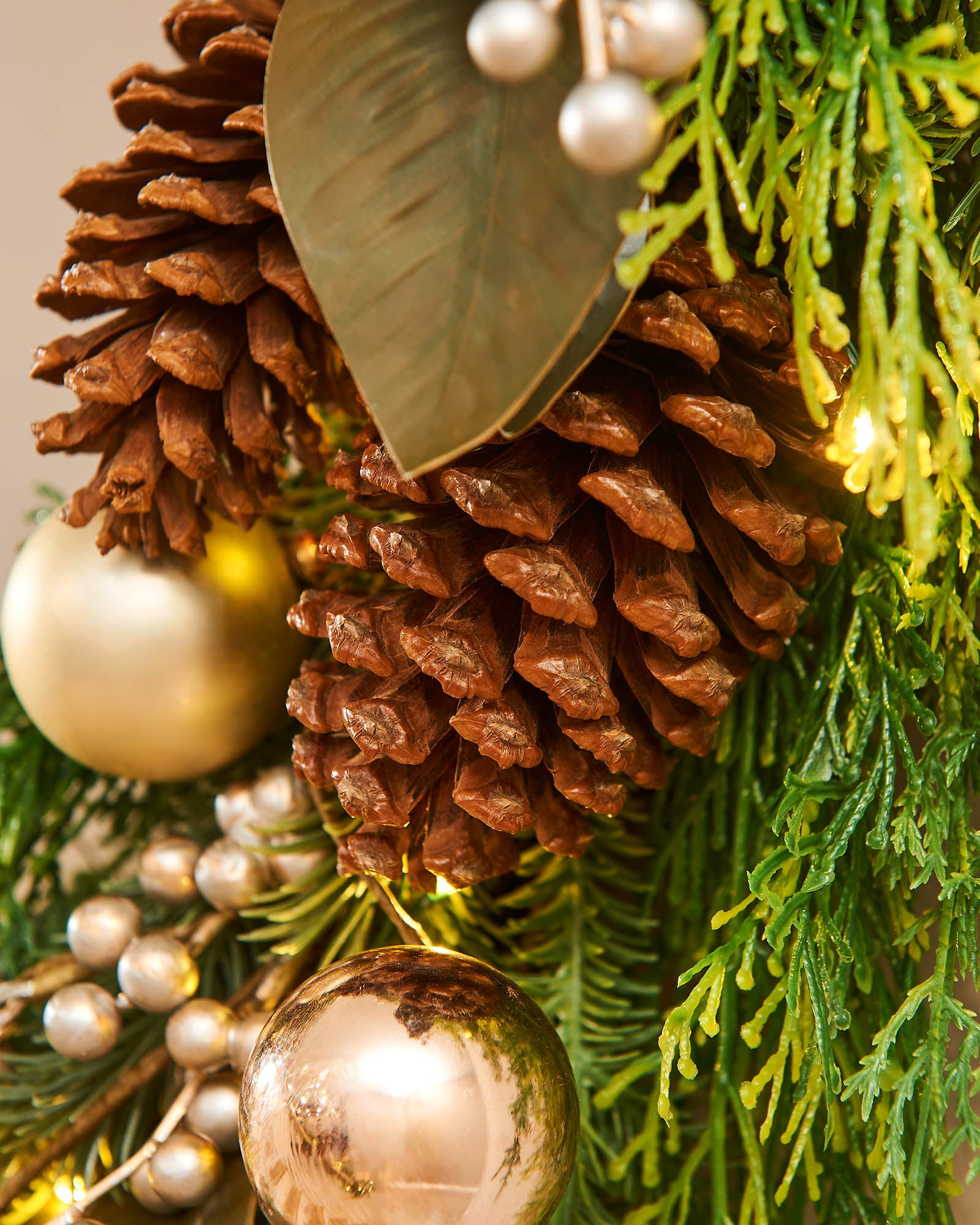 A festive Christmas wreath adorned with pinecones, gold berries, and LED lights, set against a white background.