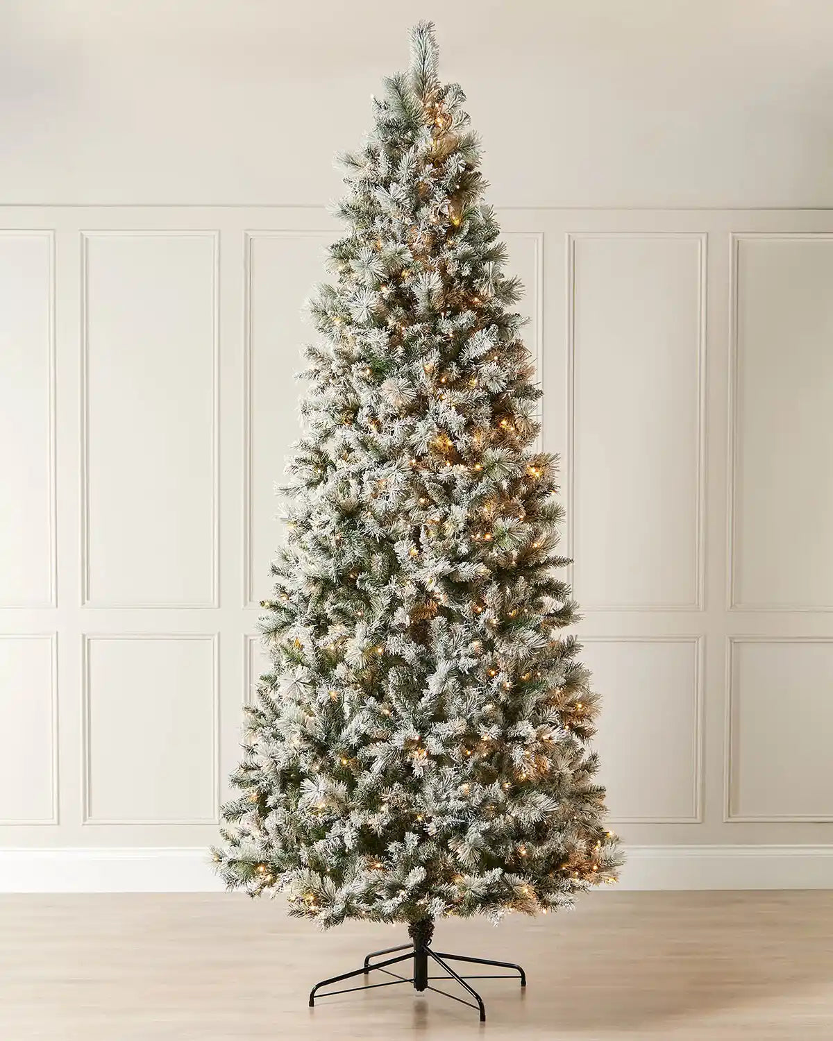 9 ft slim snow flocked spruce Christmas tree with warm white lights and black metal tree stand.