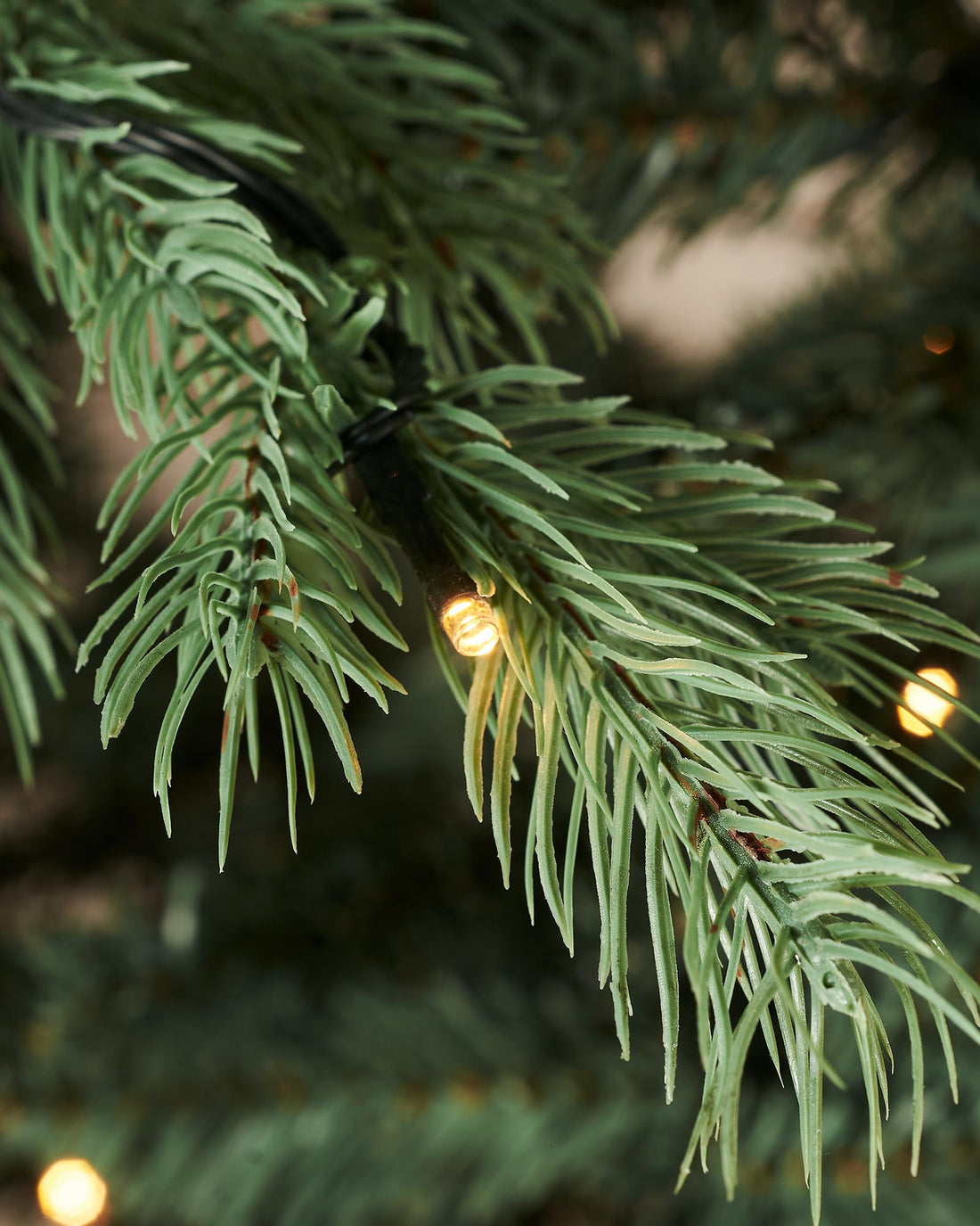 Pre-lit Colorado Blue Spruce Christmas tree with lifelike blue PE/PVC branches and built-in warm white LED lights, displayed indoors against a white wall—realistic texture, soft glow, and effortless festive elegance.