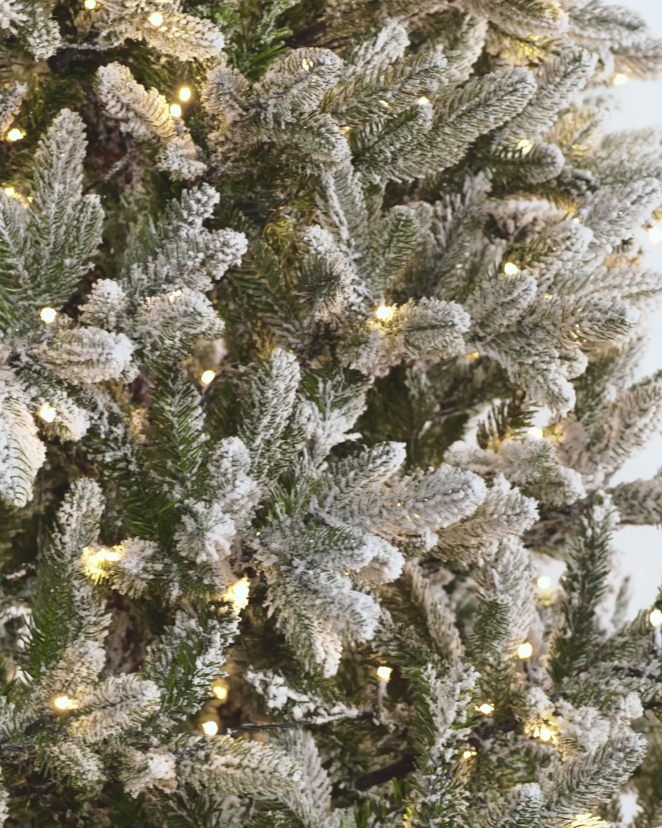 Load video: Pre-lit snow flocked Christmas tree with warm white LED lights and mixed PE and PVC branches, displayed against a white background. The tree features a realistic, snowy finish and multi-function lighting for a cozy festive look.