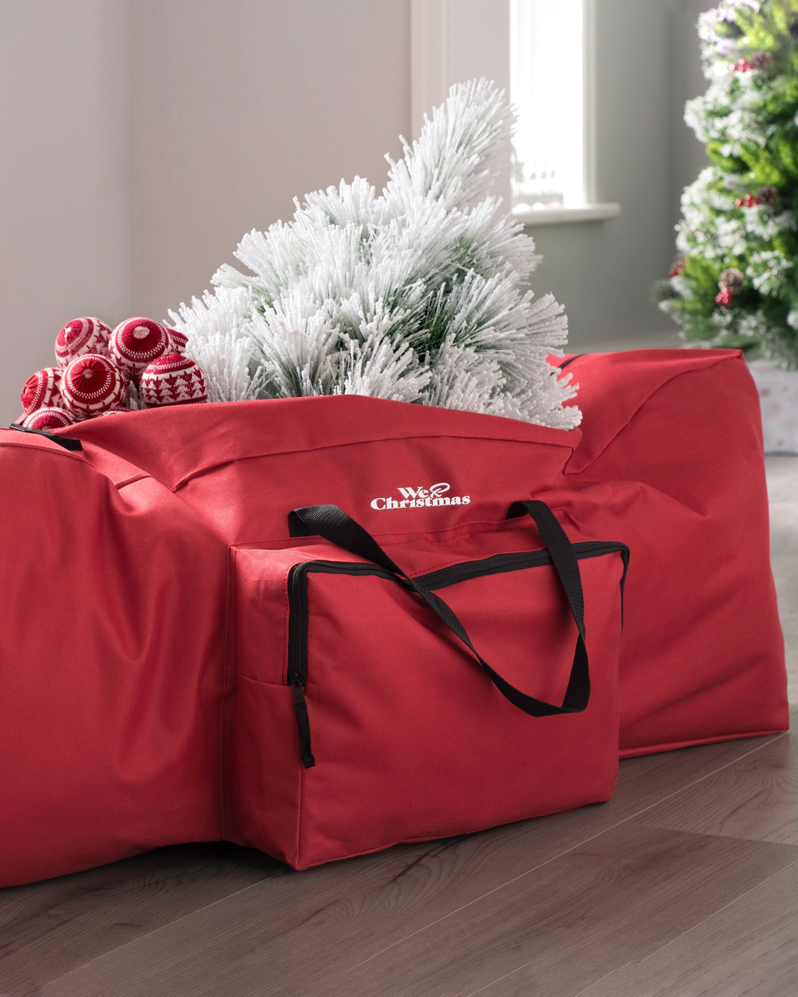 A red Christmas tree storage bag with a white artificial Christmas tree inserted into it, set against a home decor background.