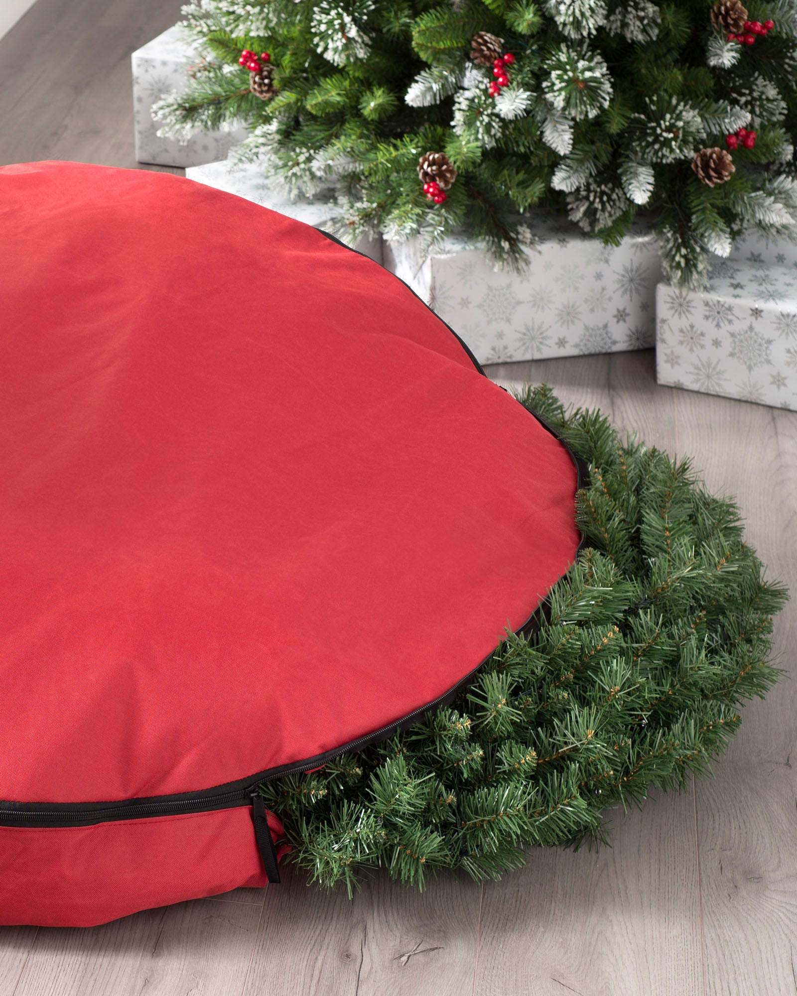 A red, extra-large garland and wreath storage bag placed next to a Christmas tree.
