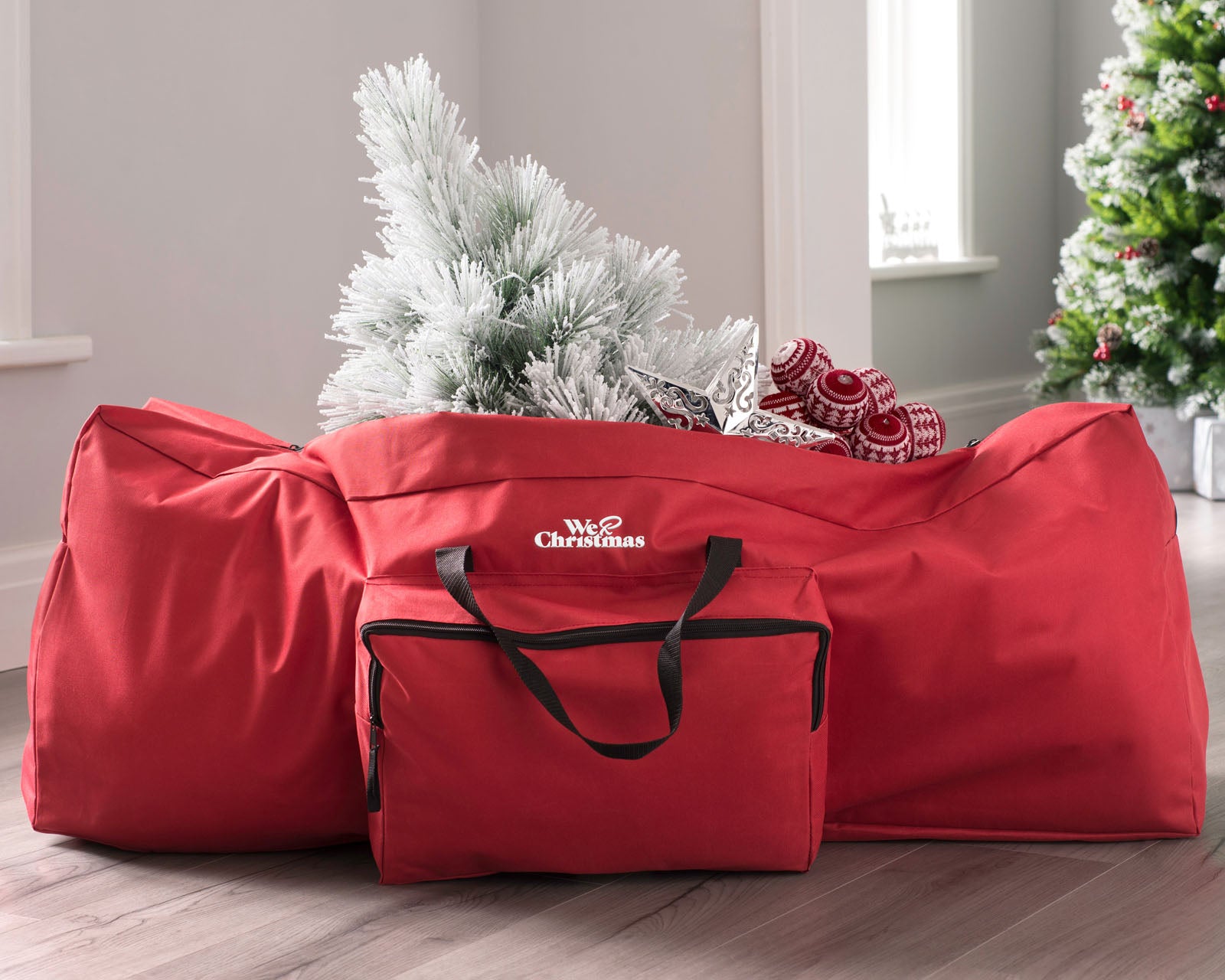 A red Christmas tree storage bag with a white artificial Christmas tree inserted into it, set against a home decor background.
