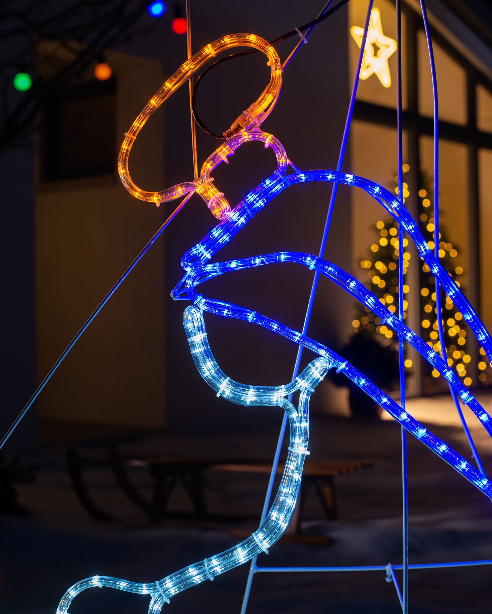 A rope light silhouette depicting baby Jesus in a manger with the bright white North Star and an angel, illuminated with multi-colored LED lights, set against a nighttime backdrop.