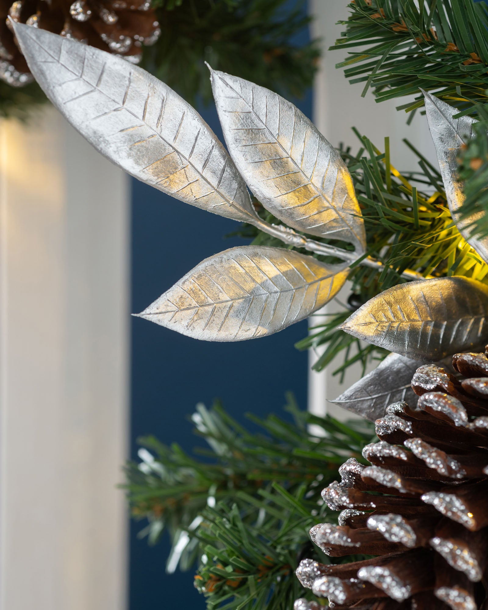 A decorated garland with silver and white elements, including LED lights, pinecones, and faux flowers, displayed on a dark background.
