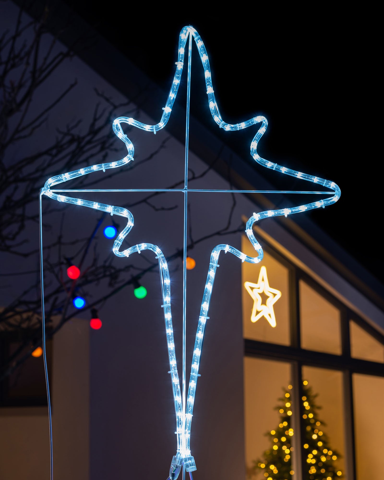 A rope light silhouette depicting baby Jesus in a manger with the bright white North Star and an angel, illuminated with multi-colored LED lights, set against a nighttime backdrop.