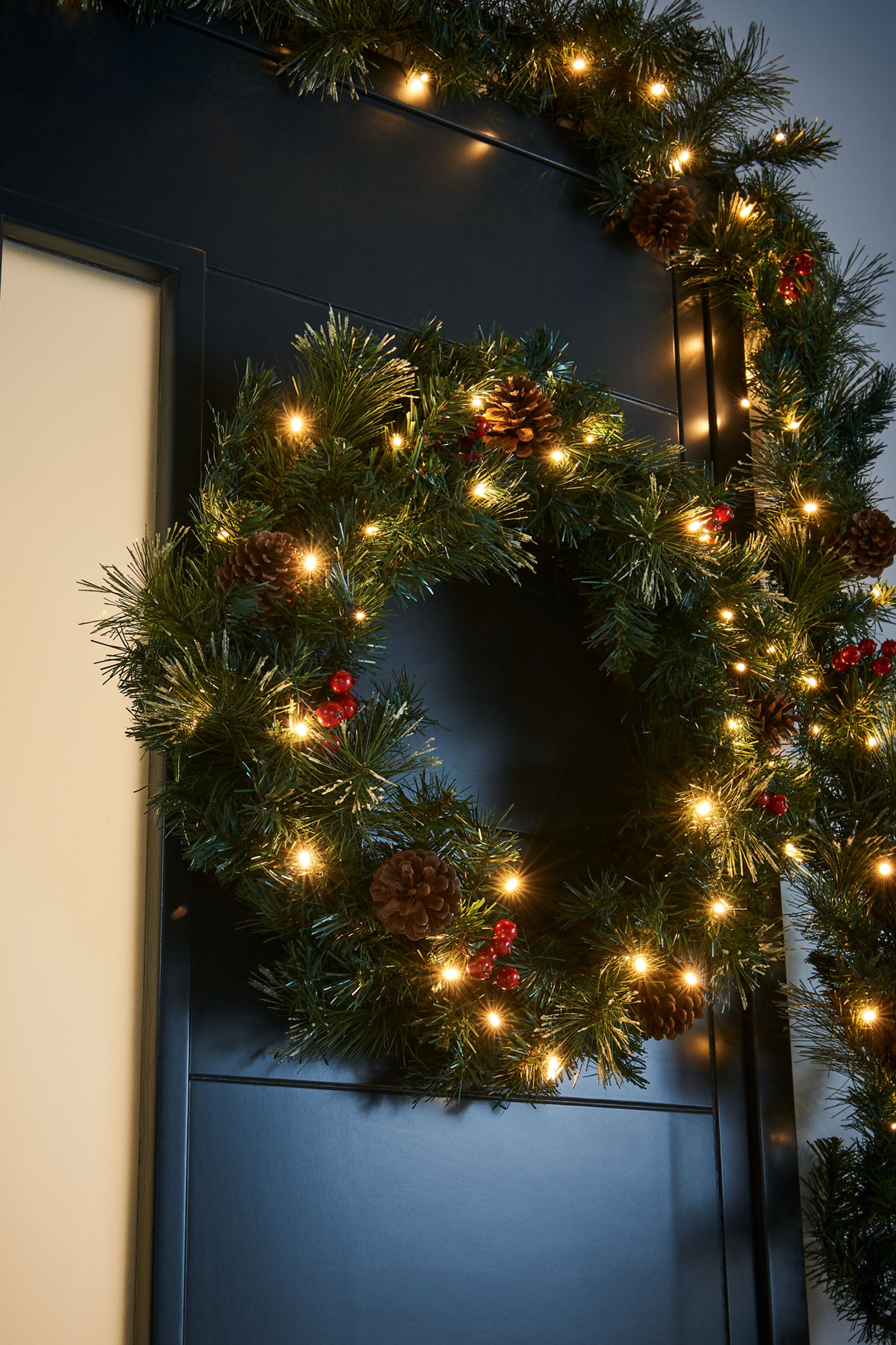 Pre-lit Christmas decoration set including two potted trees, a wreath, and a garland—all featuring warm white LED lights, red cluster berries, pinecones, and frosted PVC tips—ideal for creating a coordinated festive display at a home entrance.