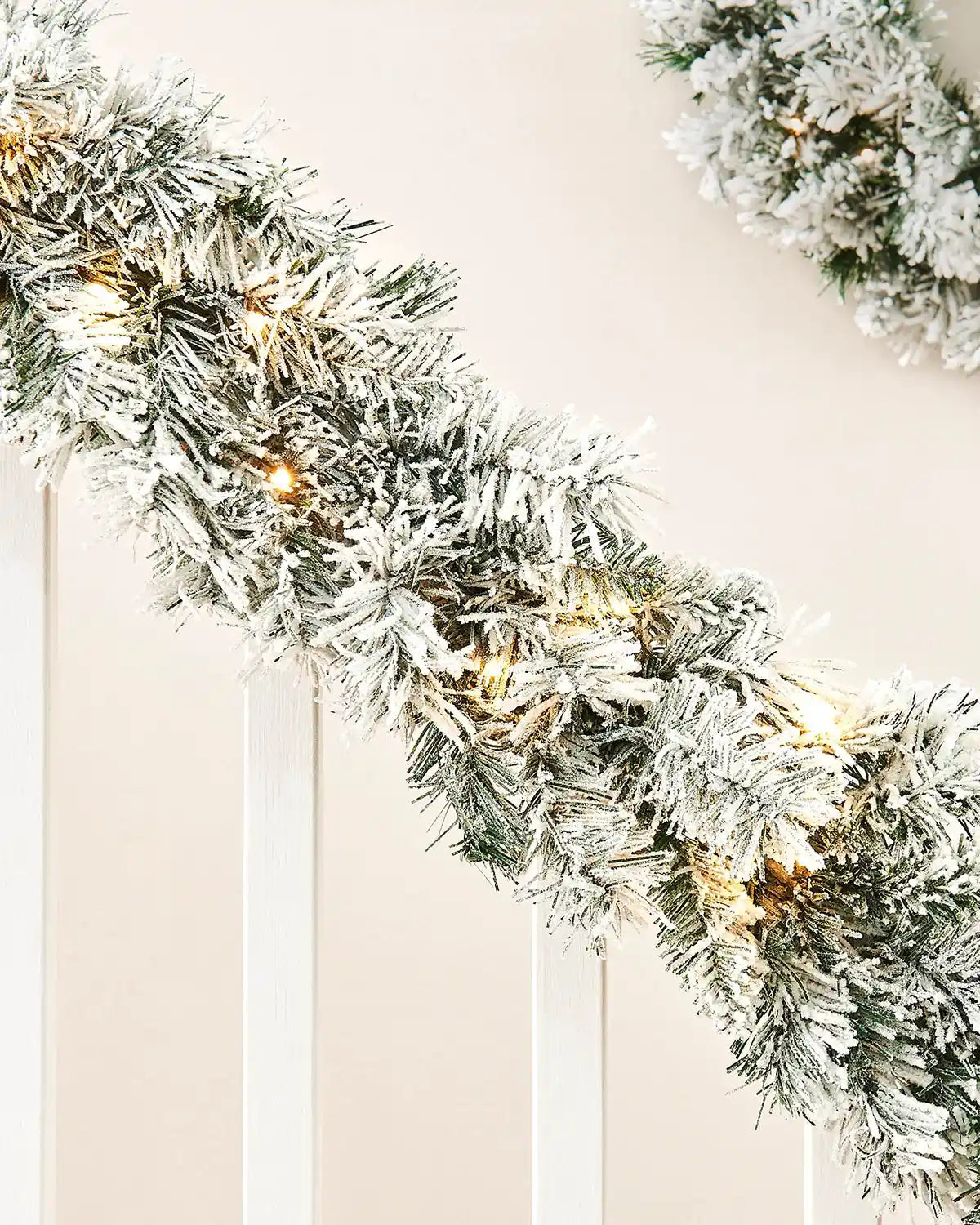 Close-up of a 9ft snow-flocked spruce garland with warm white lights wrapped along a white staircase