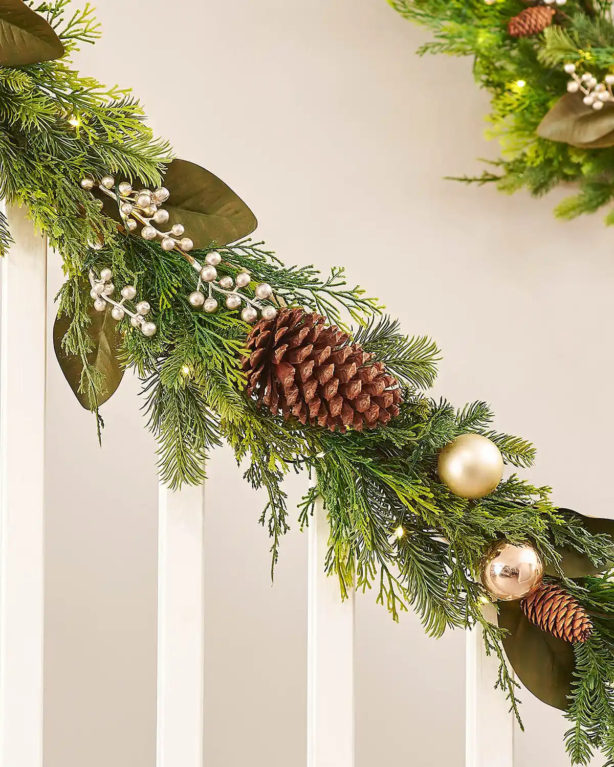 Decorative Christmas garland with pine cones and ornaments on a staircase banister against a neutral background