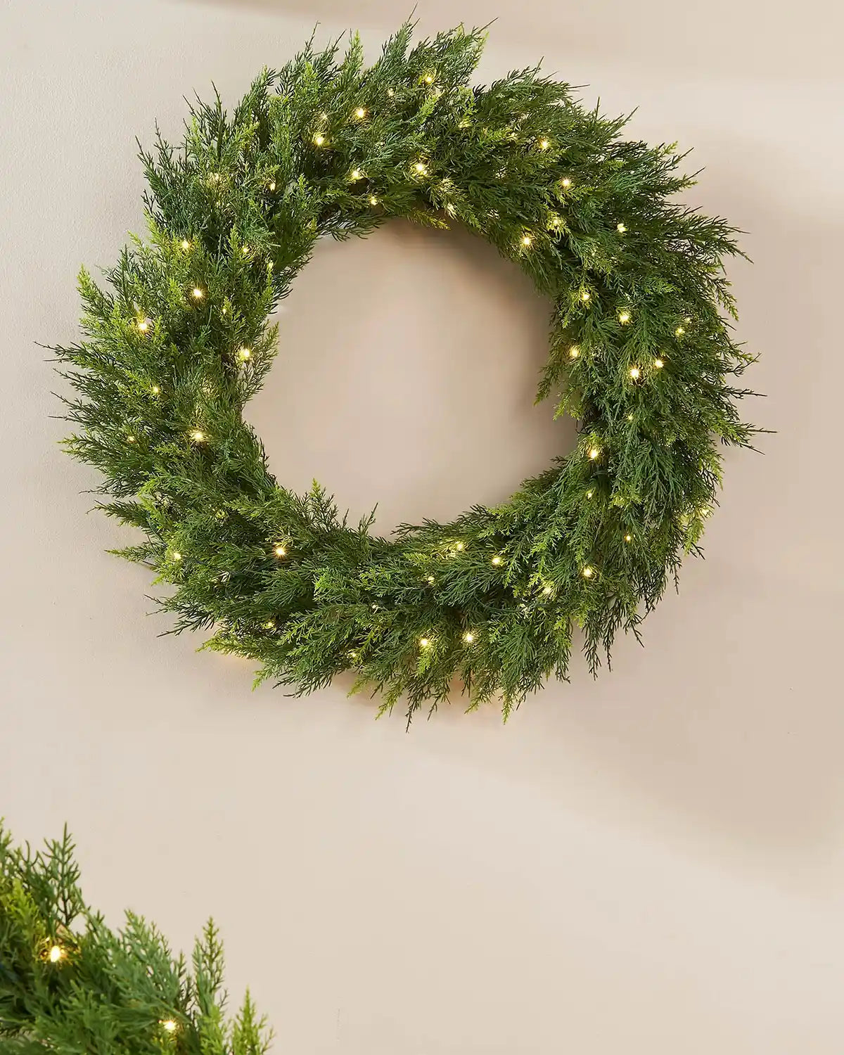 Full looking green wreath with warm white lights on a cream wall
