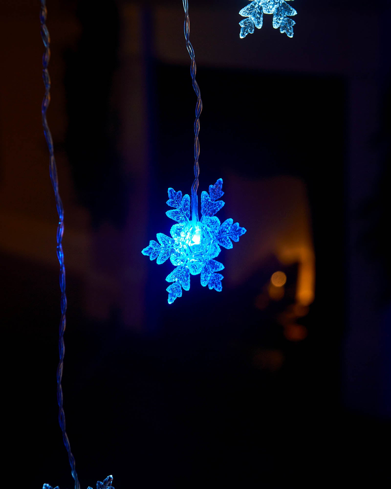 Blue illuminated snowflake detail on a hanging curtain light strand
